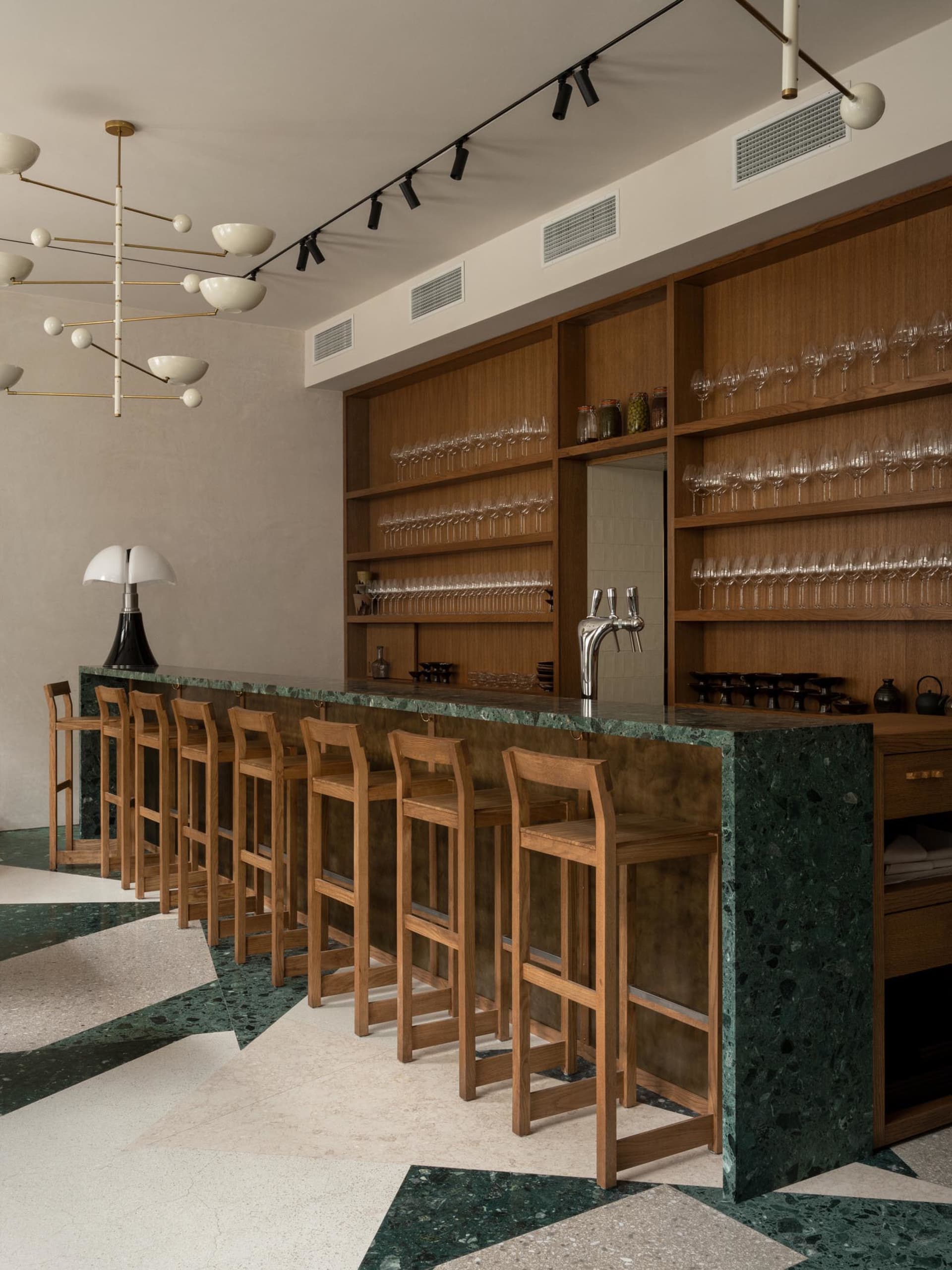 A sophisticated bar area with a marble countertop, wooden stools, and wine glasses, set in a restaurant with an elegant atmosphere