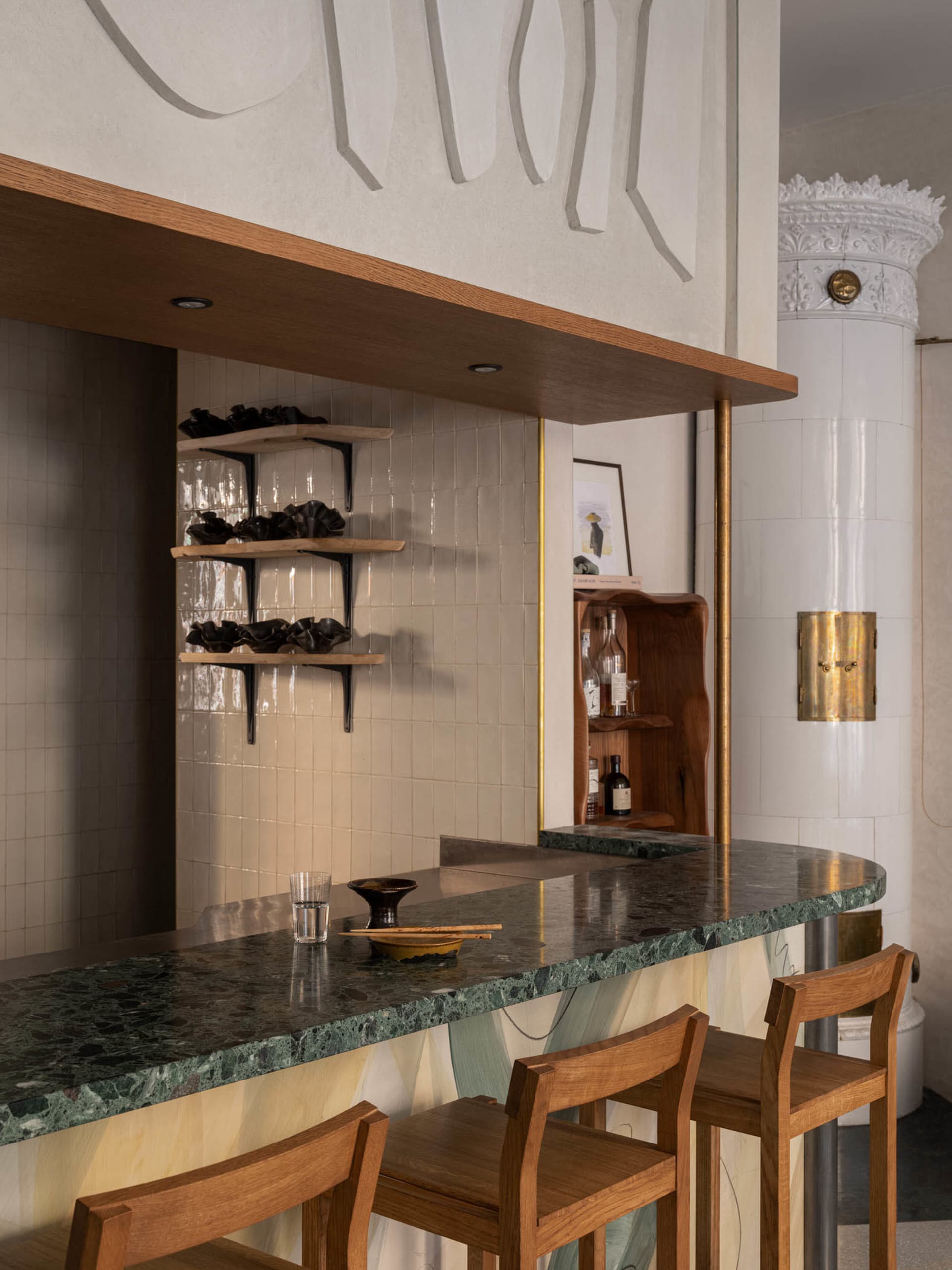 Elegant bar area with a marble countertop, a wooden chair, wine glasses, a bowl, and a bottle, set in a sophisticated atmosphere