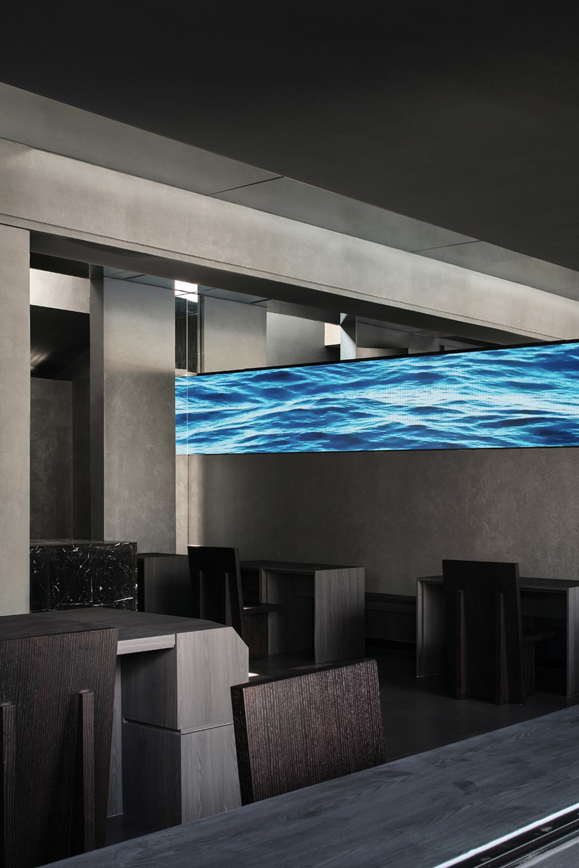 Modern restaurant interior with a large screen TV above a dining table, surrounded by chairs and a comfortable seating area