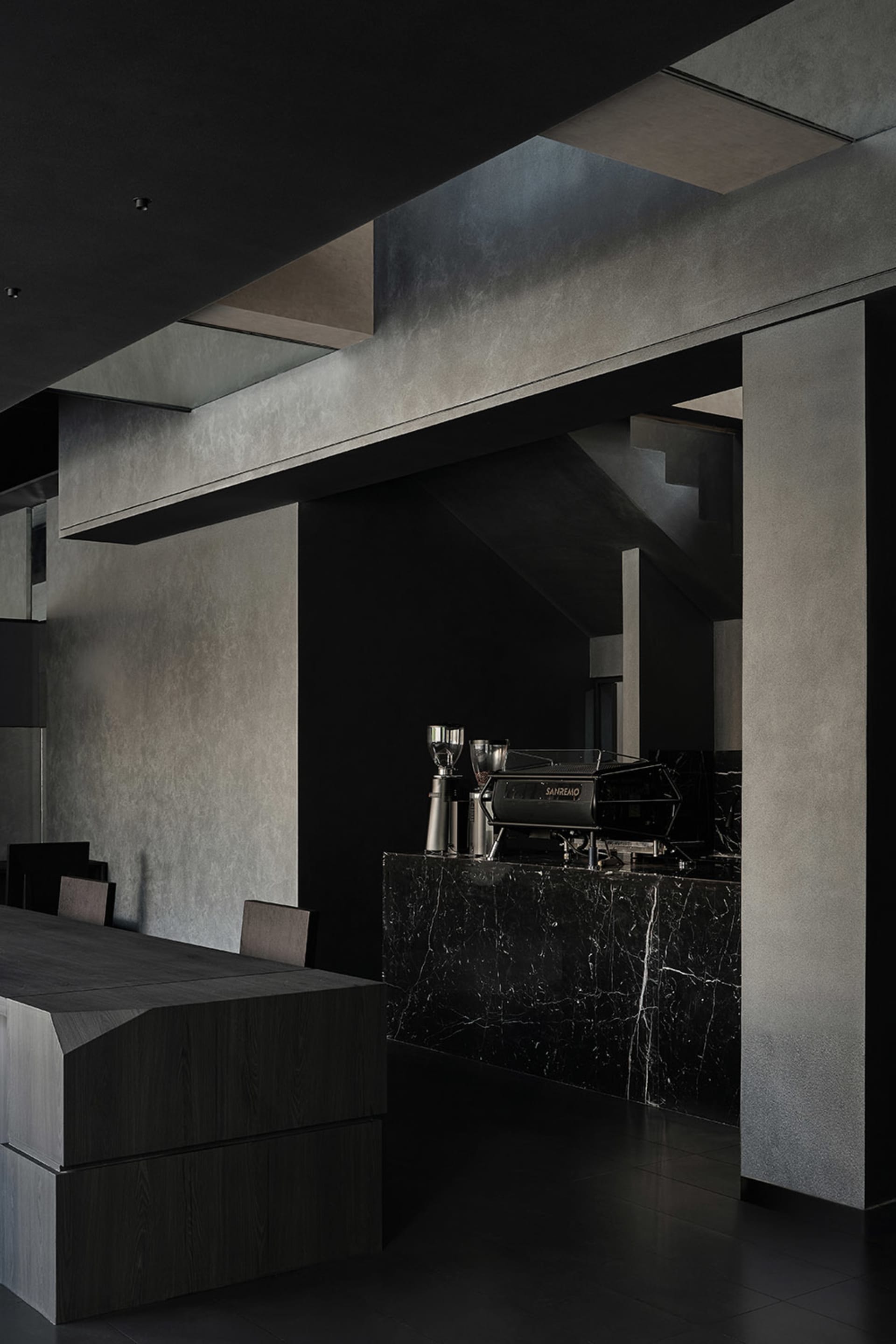 A dark and moody coffee shop interior with a black countertop, coffee machine, and cups, suggesting a nighttime setting