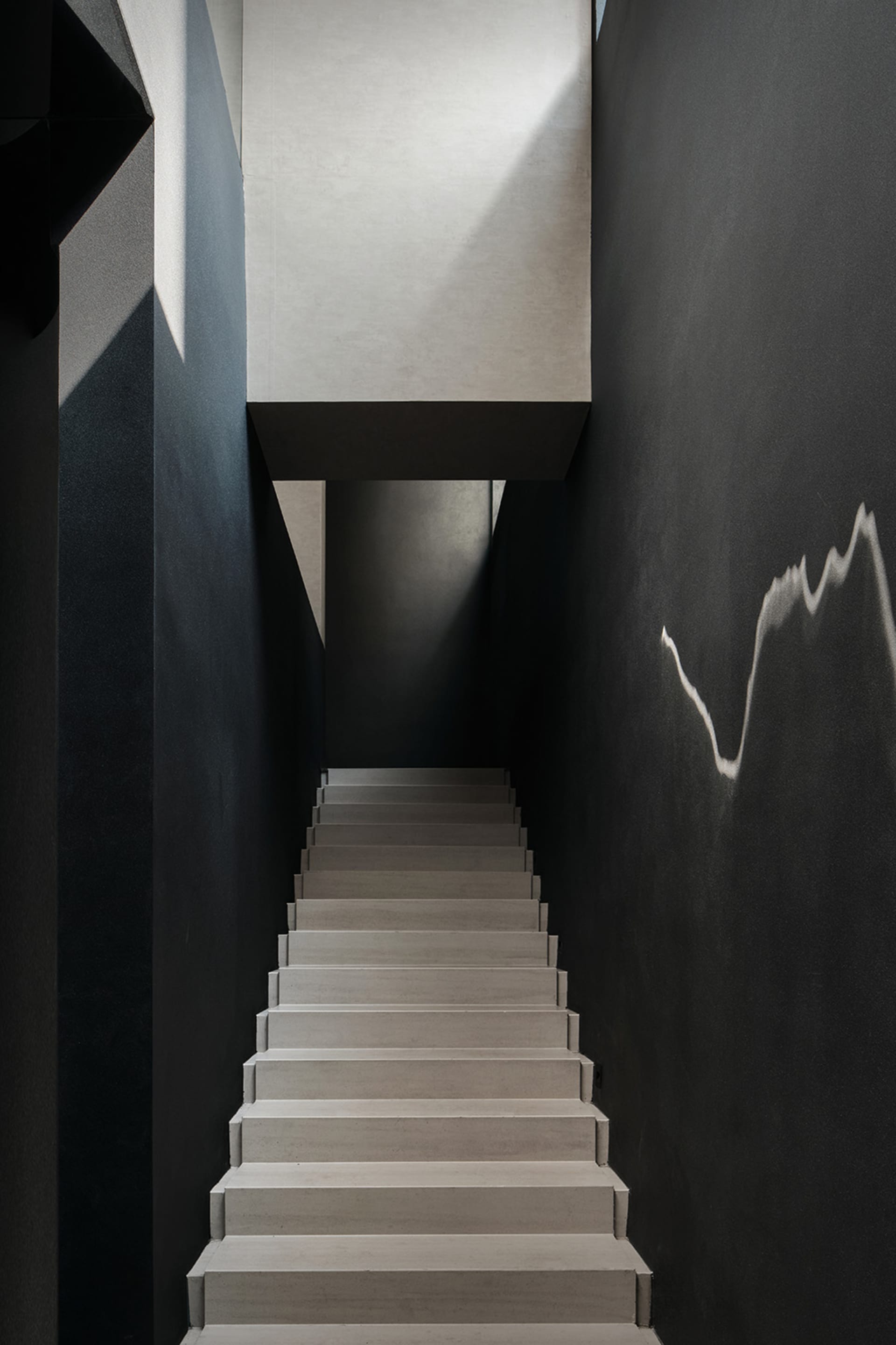 A darkened space with a concrete staircase and black railing, featuring several steps leading upwards