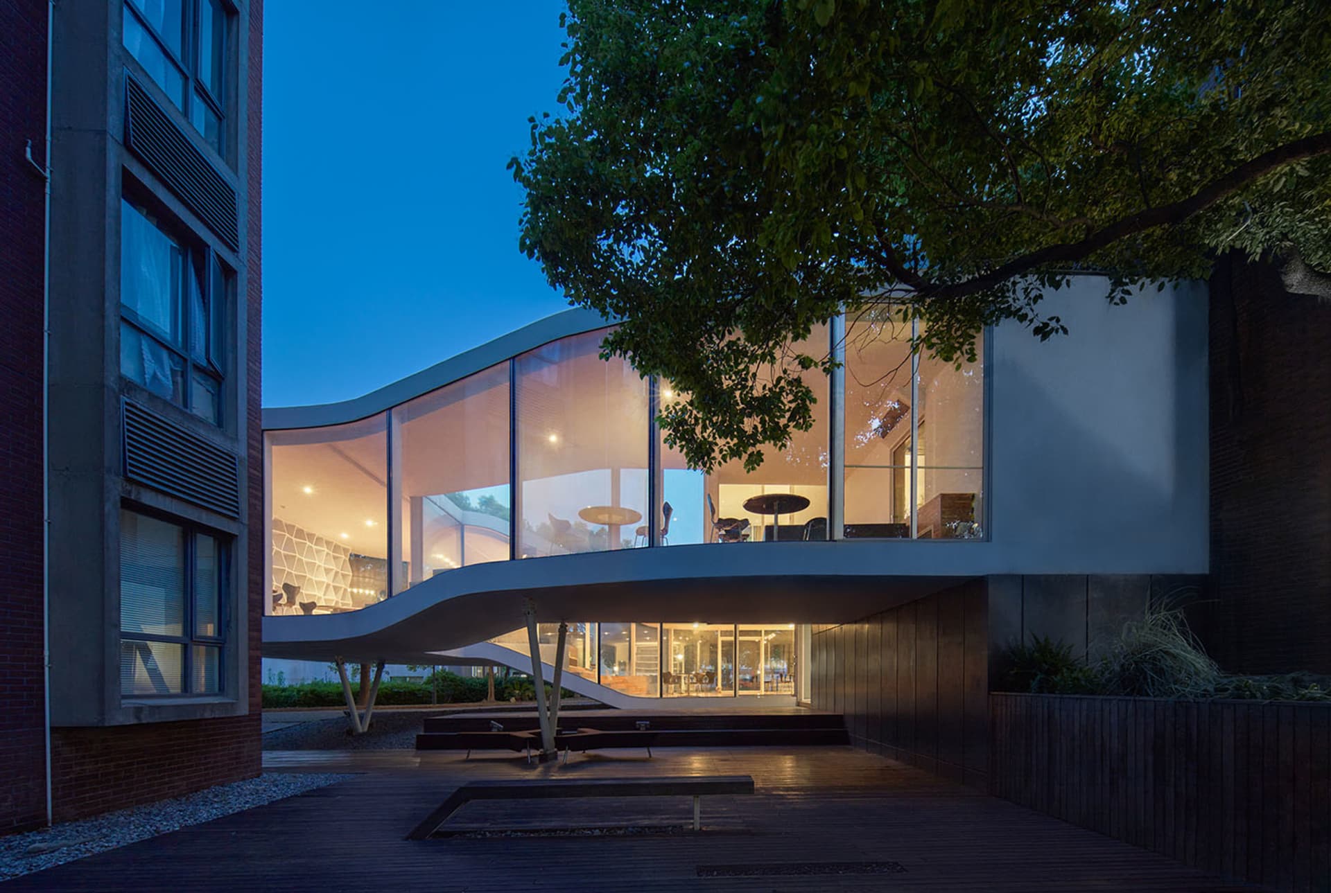 Modern building with a large glass wall and outdoor seating area with chairs and benches