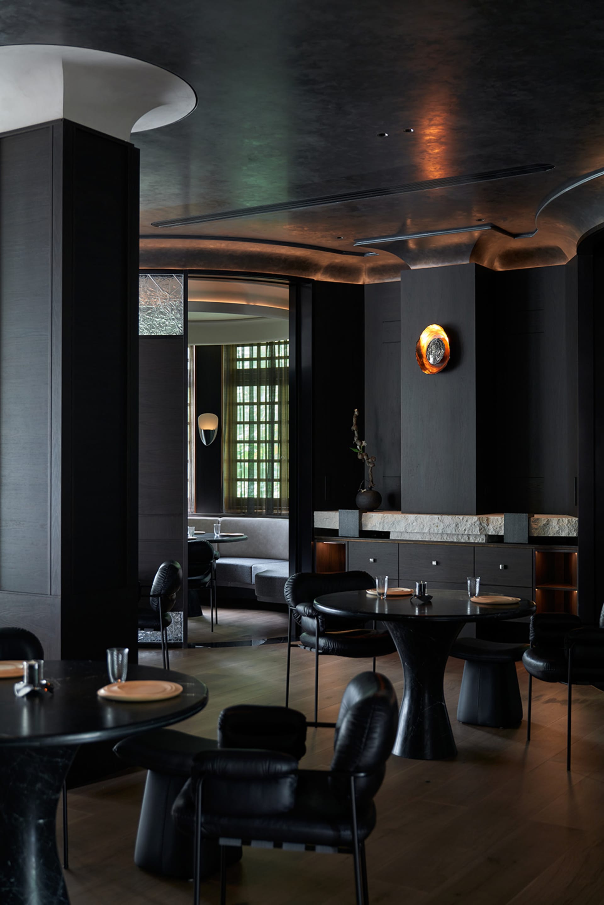 Modern restaurant interior with multiple tables, chairs, potted plants, and warm lighting