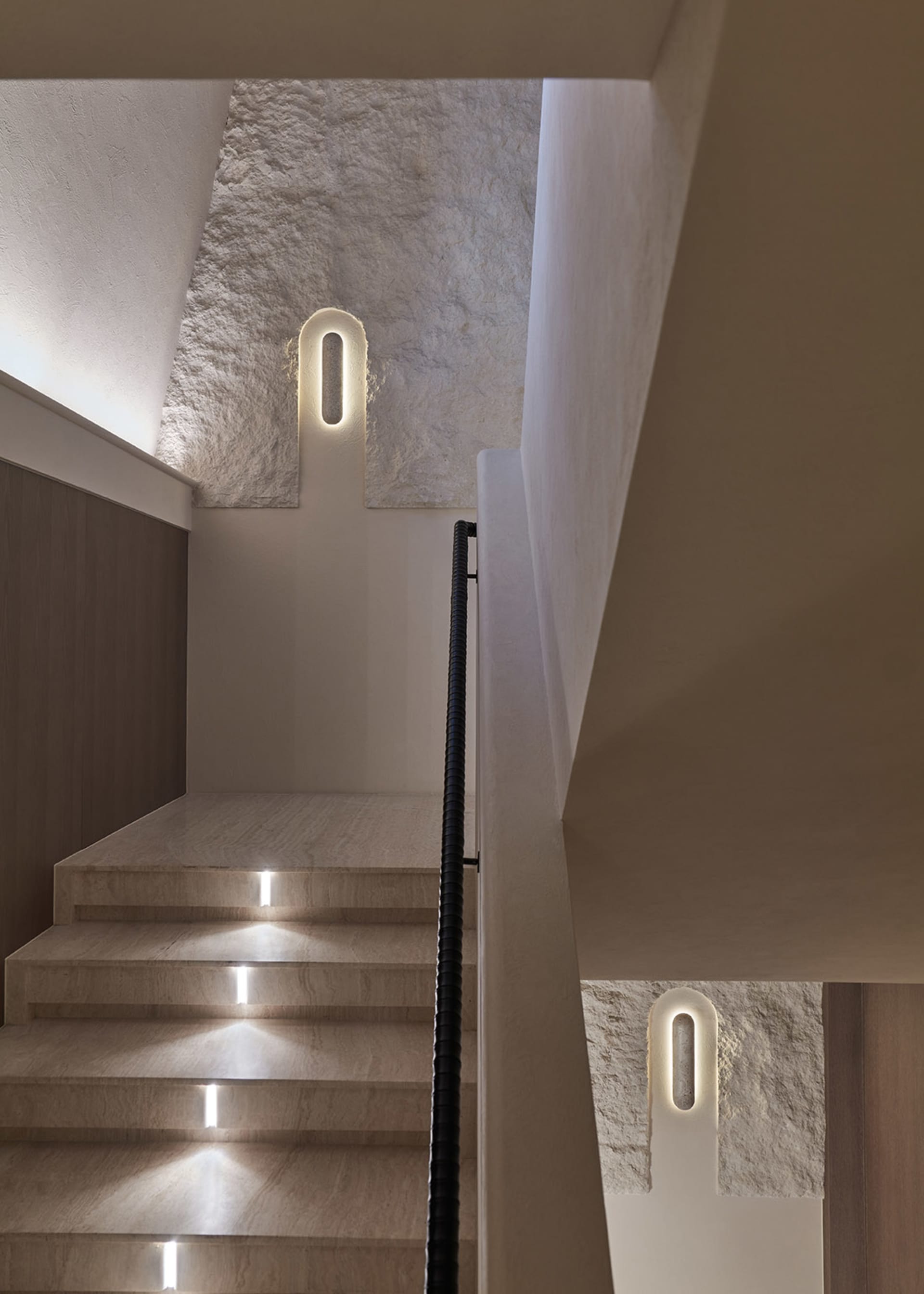 A staircase in a house with wooden railing and stone-like steps, lit by two lights on each side, creating a warm and inviting atmosphere