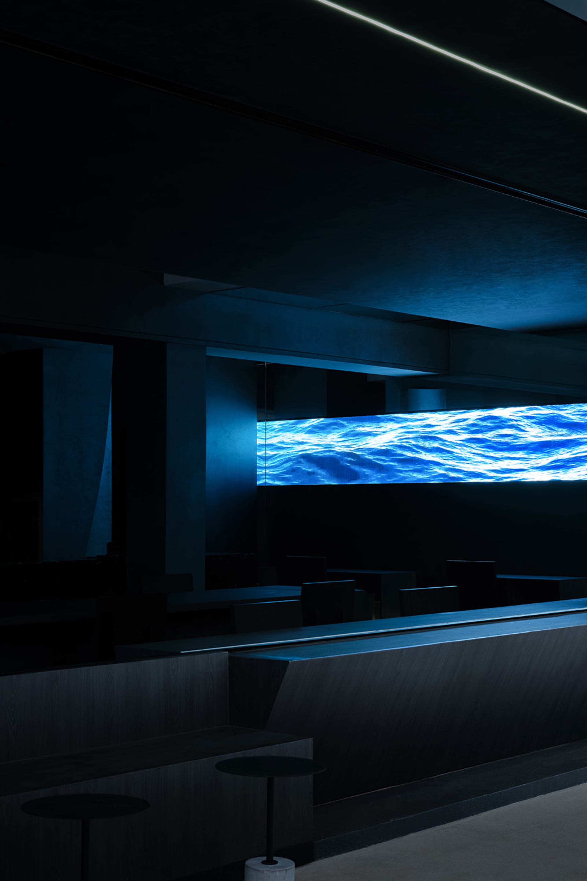 A darkened restaurant with a large blue waterfall as its centerpiece, surrounded by empty chairs and a sense of relaxation