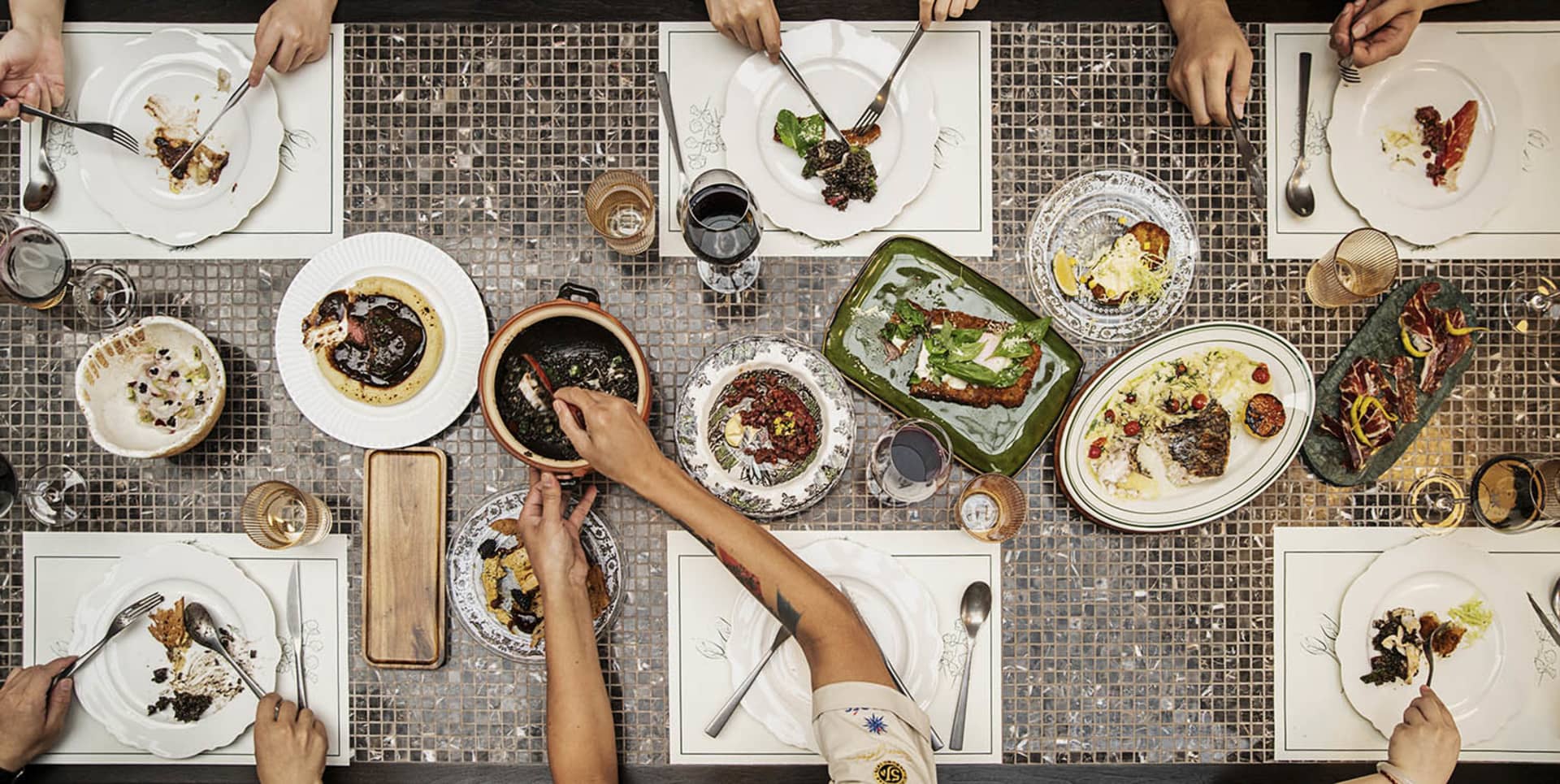 A warm and inviting dining scene with a wooden table, chairs, and various plates of food, wine glasses, and utensils
