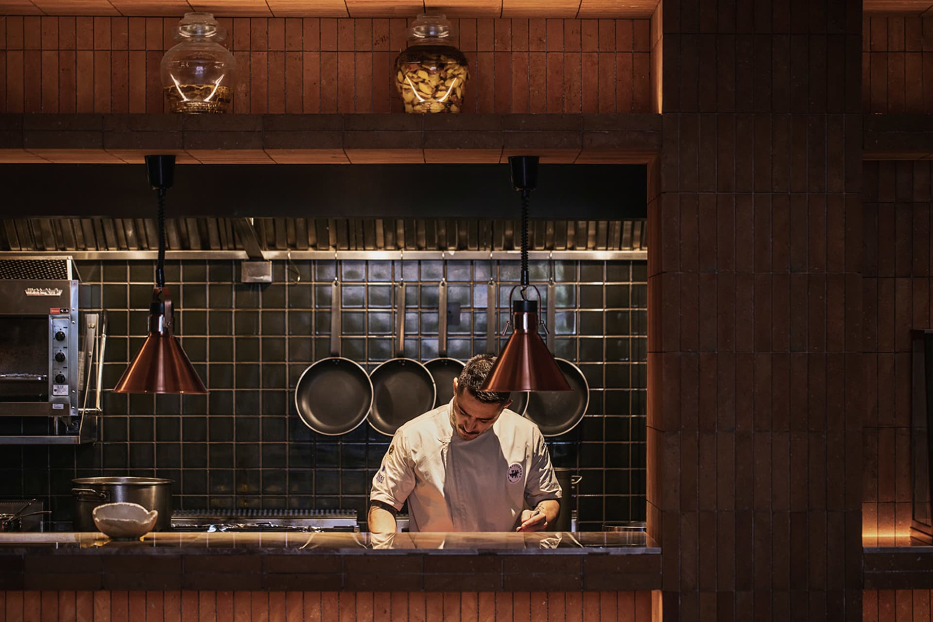 A man prepares food on a kitchen island with various cooking utensils and ingredients nearby