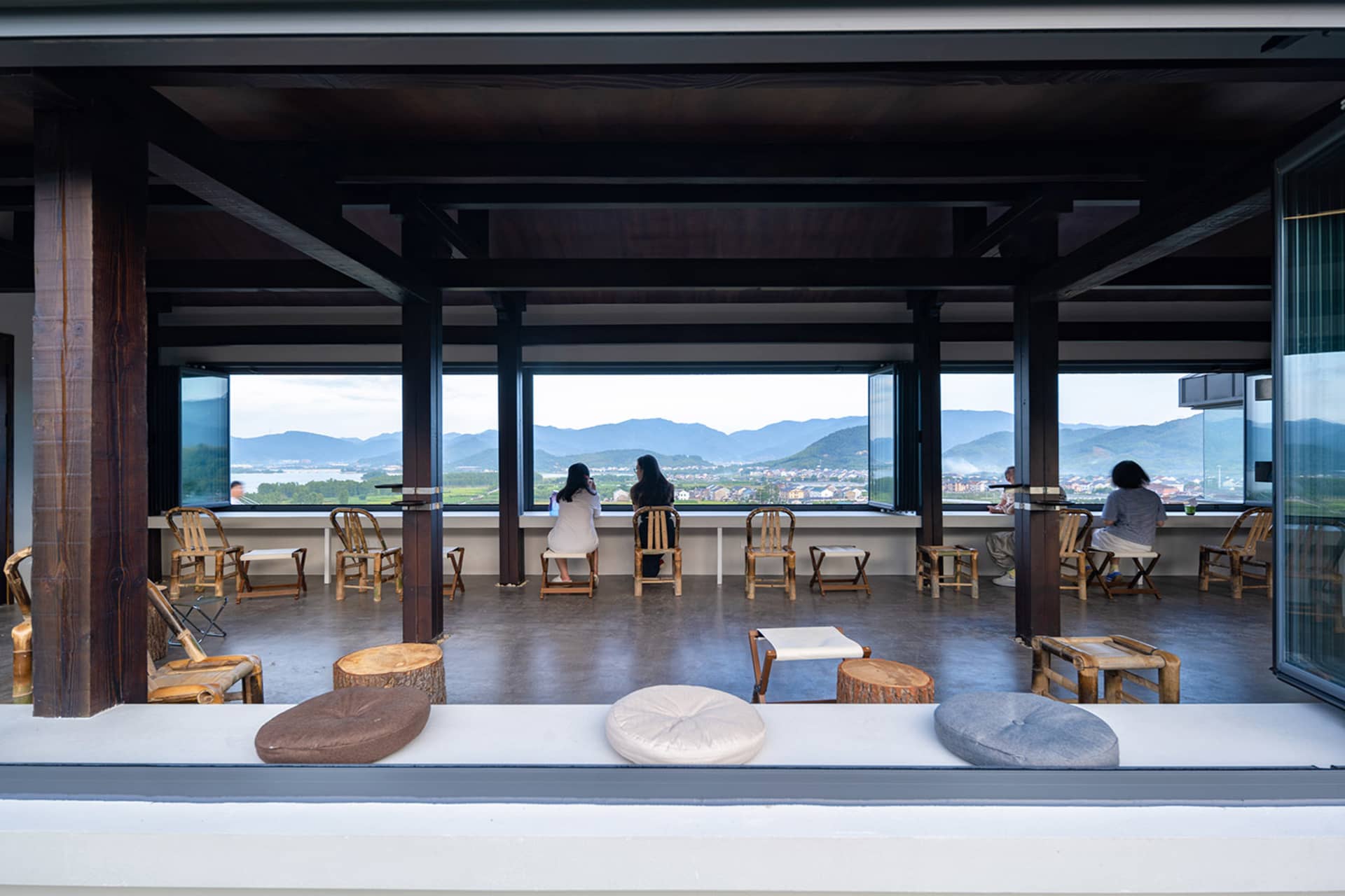 Outdoor dining area with wooden furniture, tables, and chairs, surrounded by a mountain landscape with a relaxed and inviting atmosphere