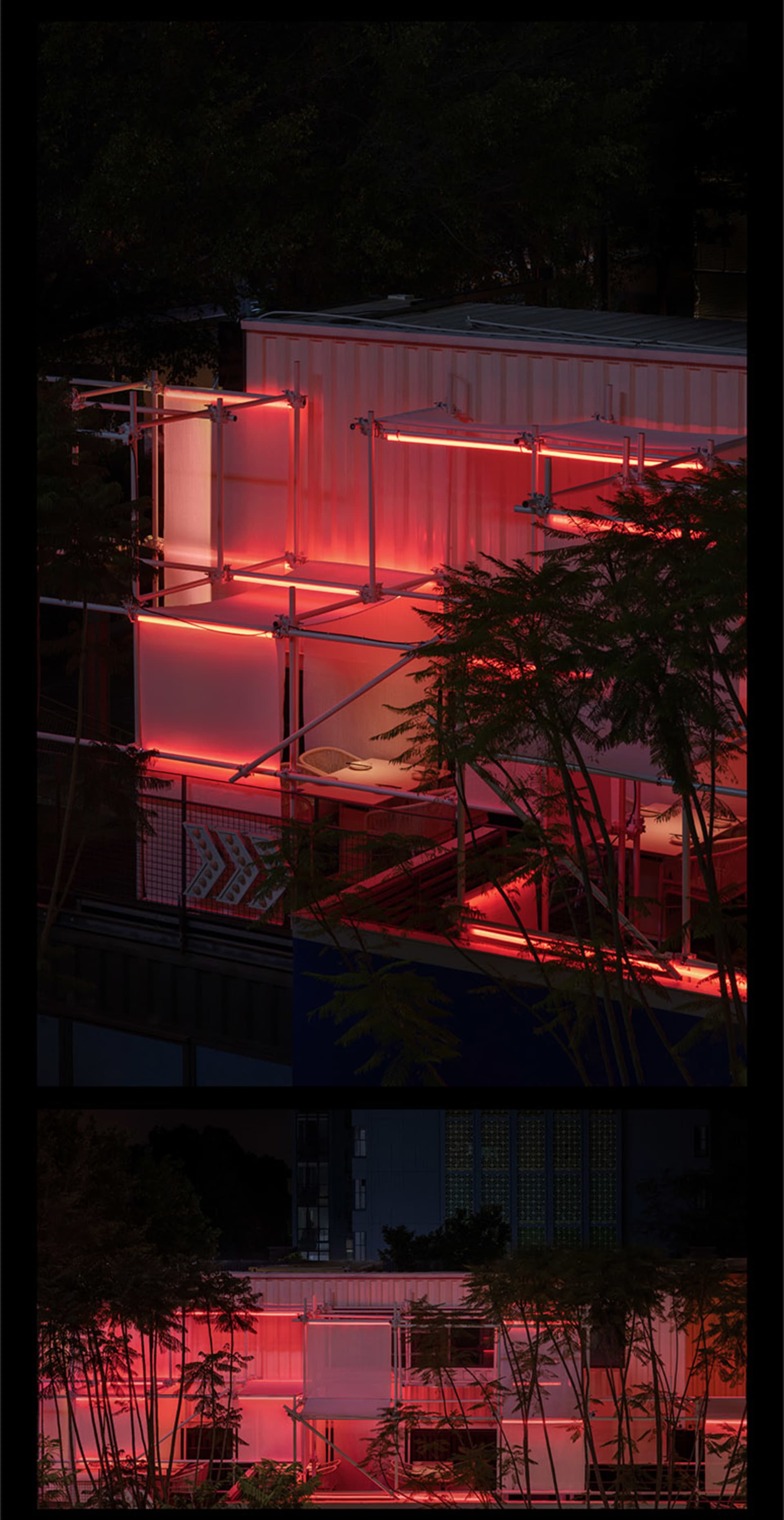 A modern building at night with red lights illuminating its exterior, featuring multiple levels and a balcony, with two chairs in front for outdoor seating or event setup