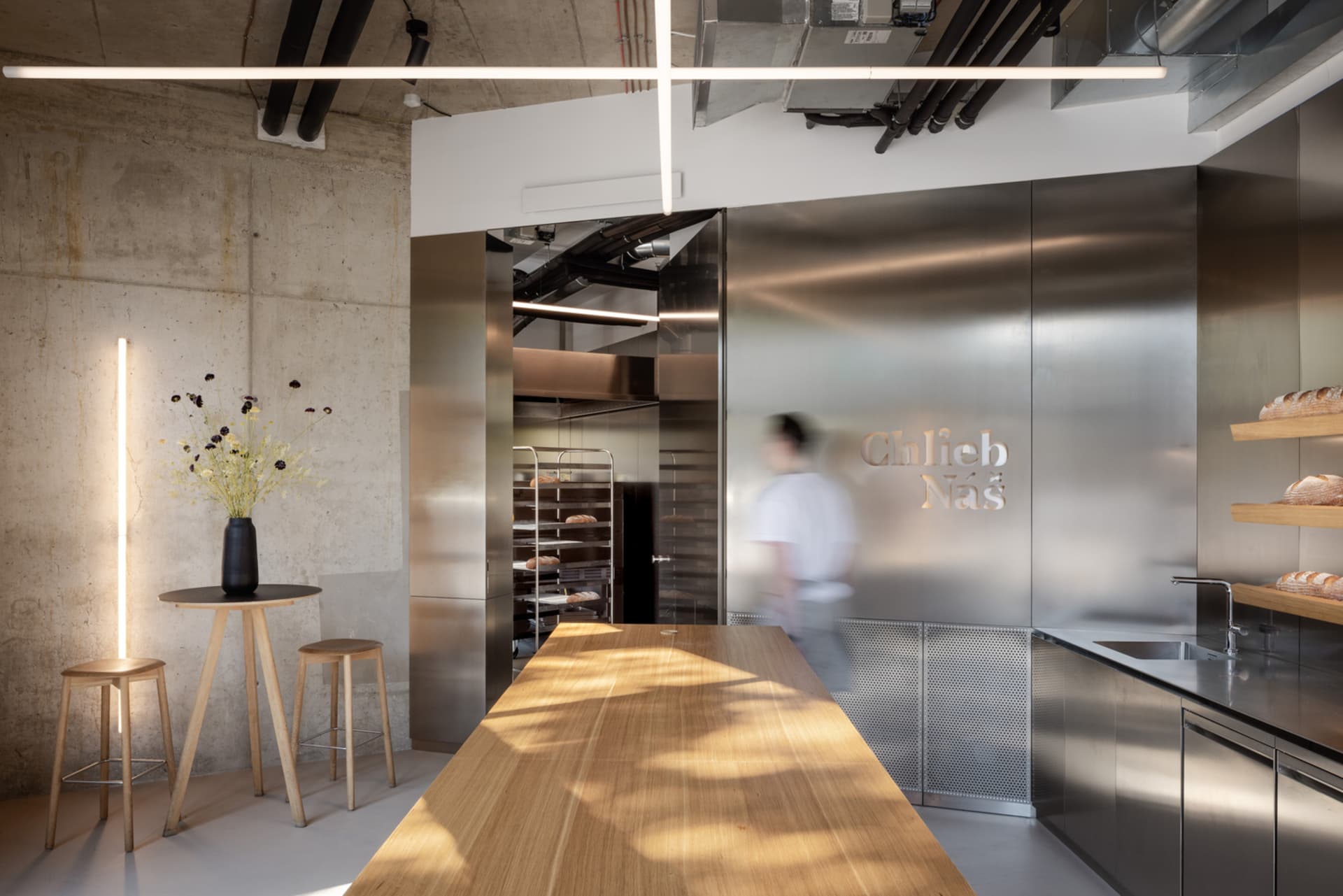 A modern kitchen with a wooden table and two ovens, surrounded by chairs, in a well-lit space with a focus on functionality and aesthetics
