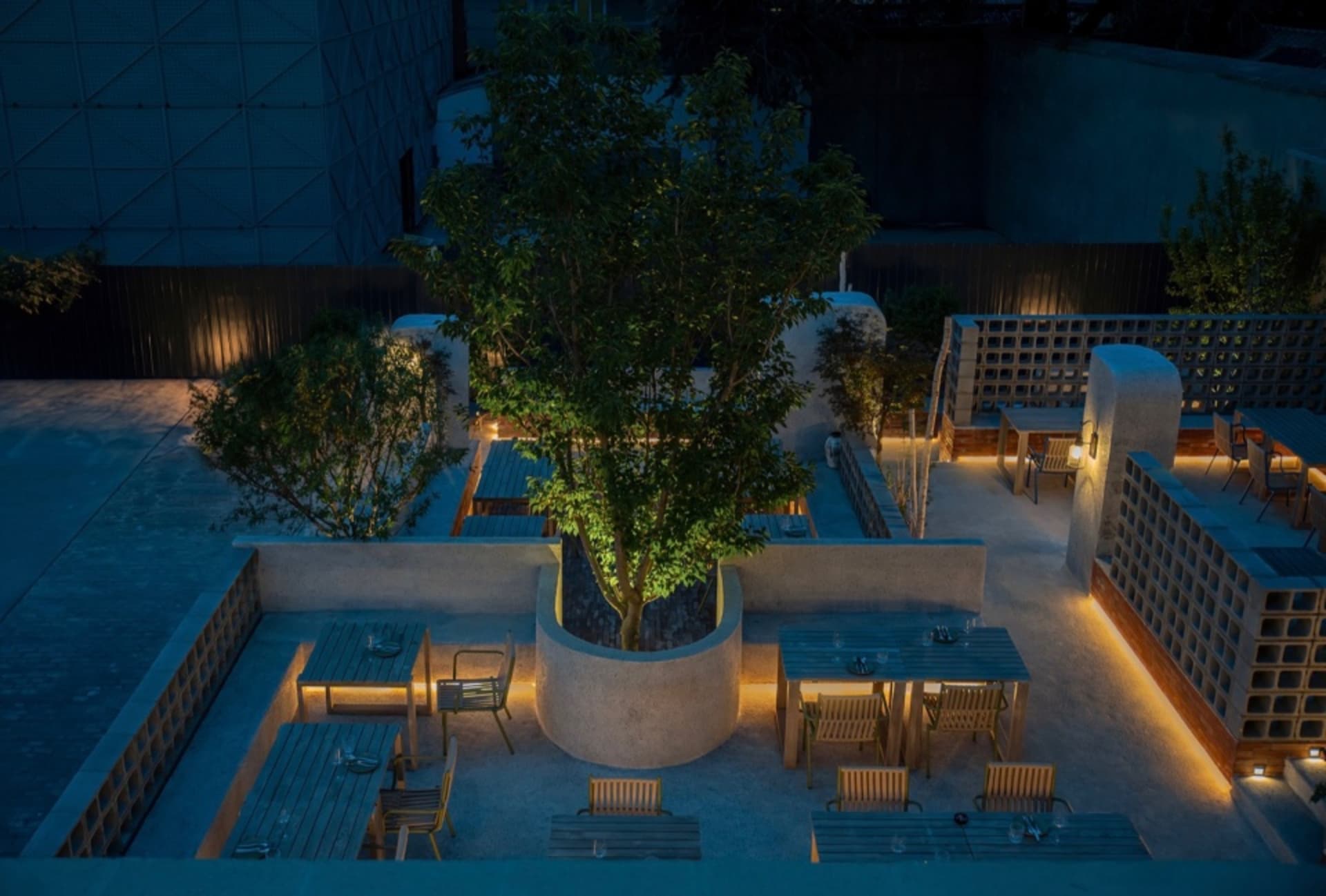 A patio area with tables and chairs arranged around a central tree, creating an inviting space for dining and socializing