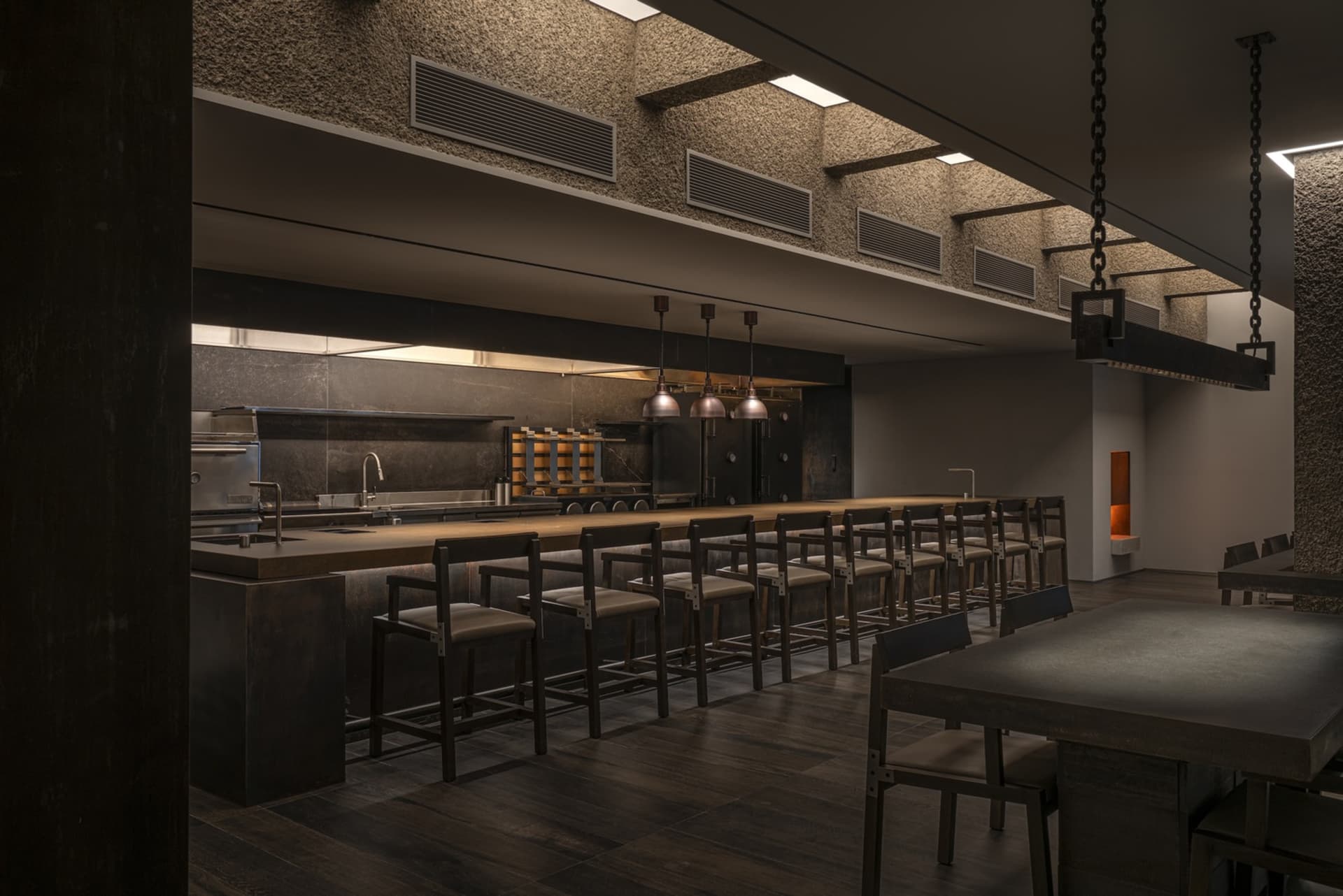 Dark and empty restaurant with a long bar counter and chairs, dimly lit with bottles on the counter
