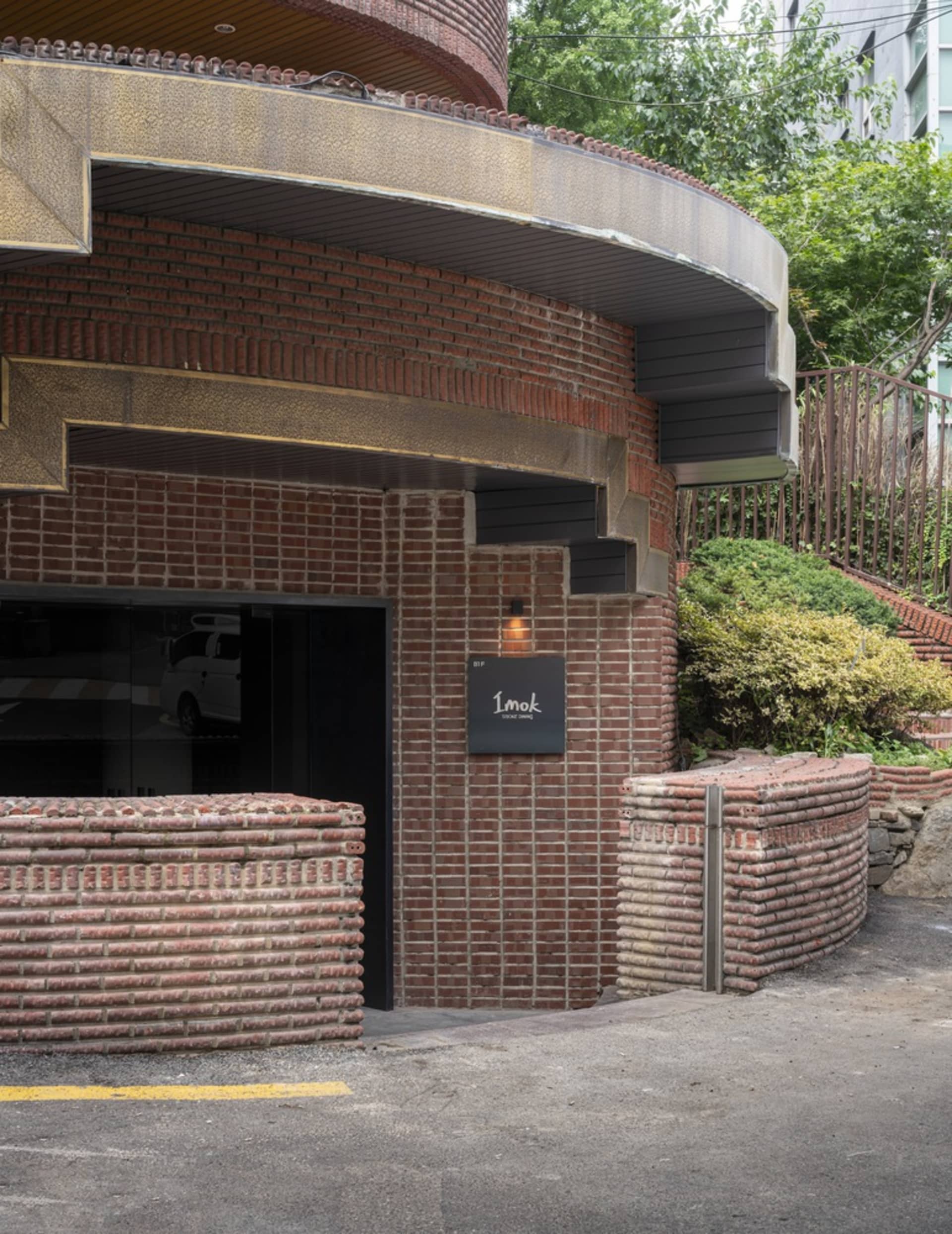 A rendered building with a brick facade, stone wall, and staircase, set against a backdrop of parked cars