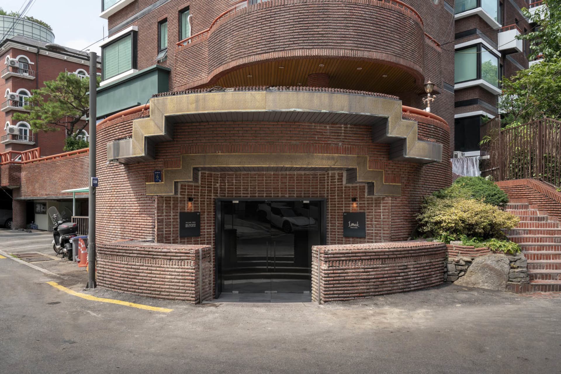 A rendered architectural scene of a building with a large brick facade, archway, and staircase, with two cars and three people in the foreground