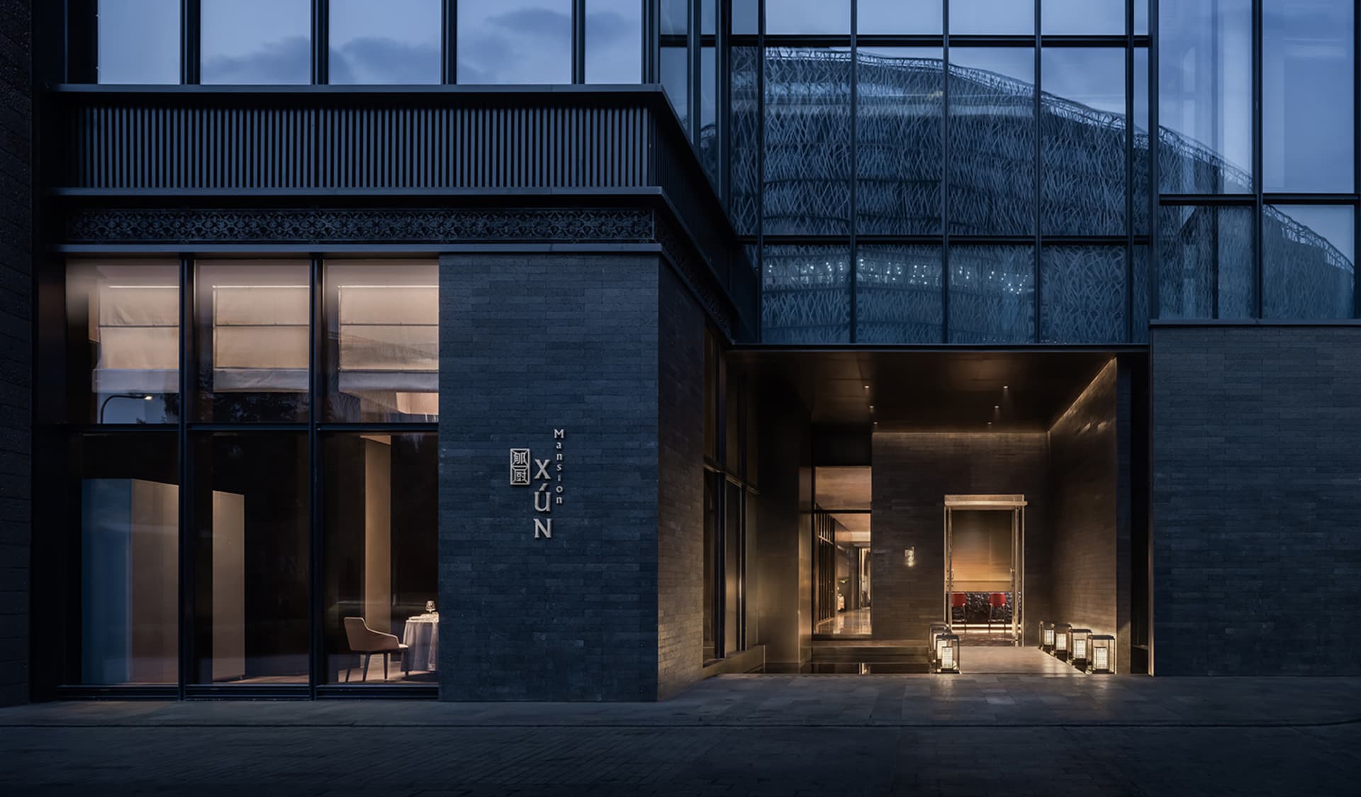 夜晚現代玻璃建築，擁有寬敞室內空間，設有座椅與餐桌，營造當代氛圍