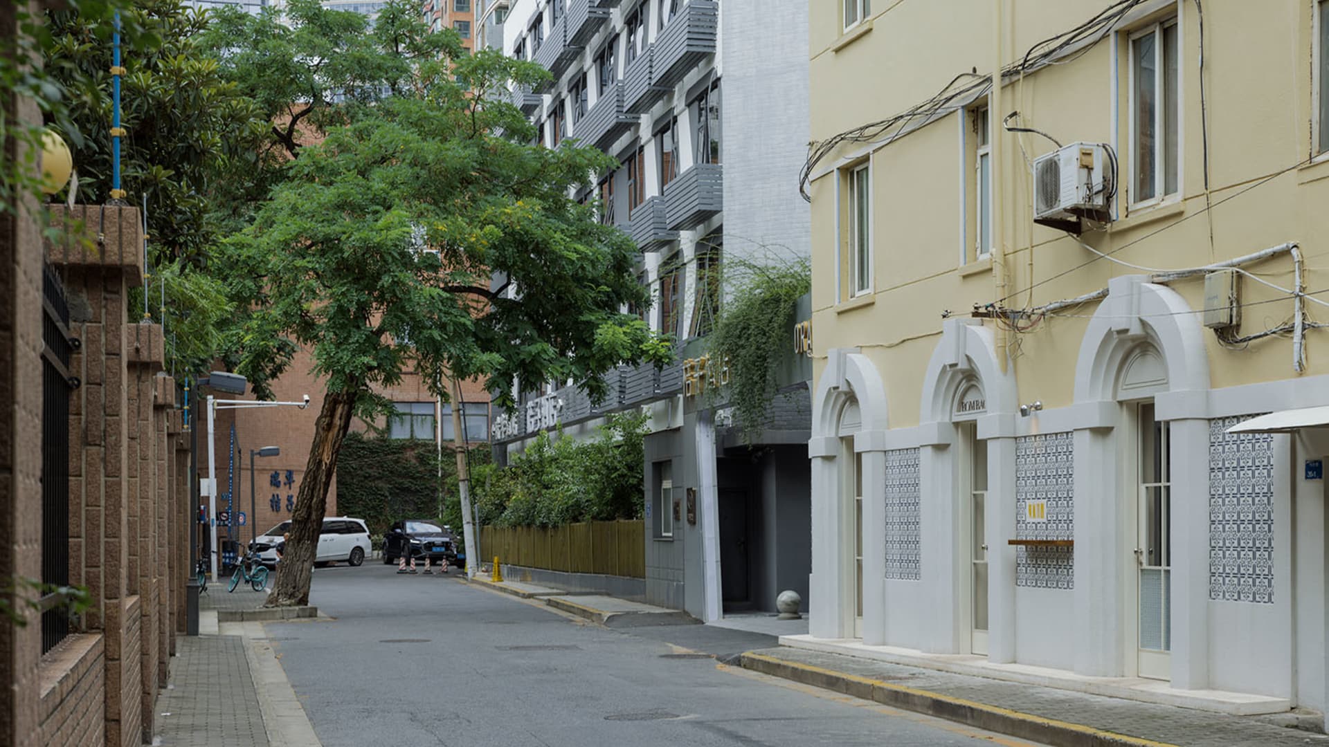 A bustling city street with a mix of architectural styles, trees, and parked cars, set against a backdrop of tall buildings