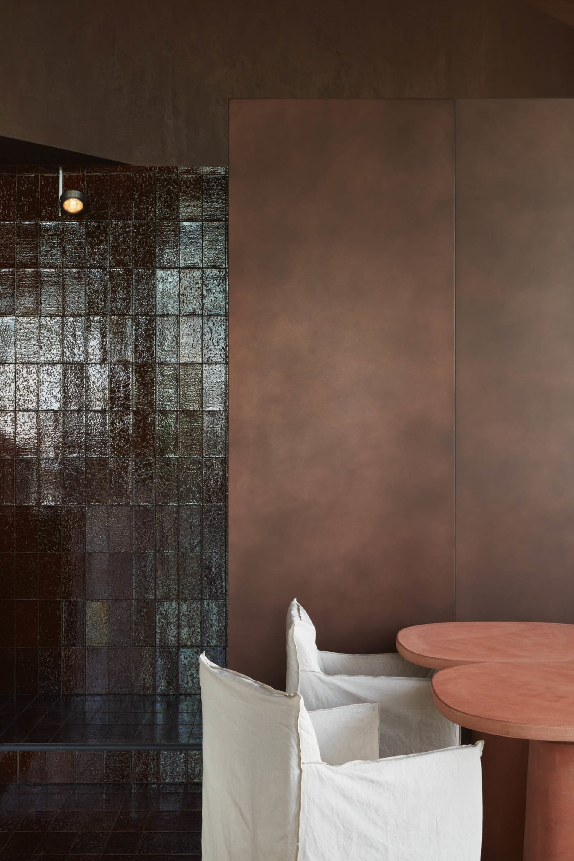 Cozy living space with a brown wall featuring a tile pattern, a dining table, and two chairs, one with a white cushion