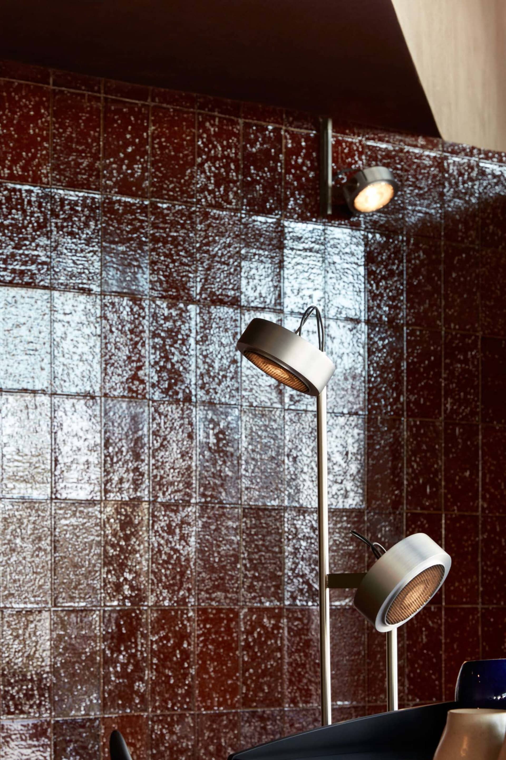 A modern room with a red brick wall featuring a tile pattern, lit by two ceiling lights, creating a warm atmosphere