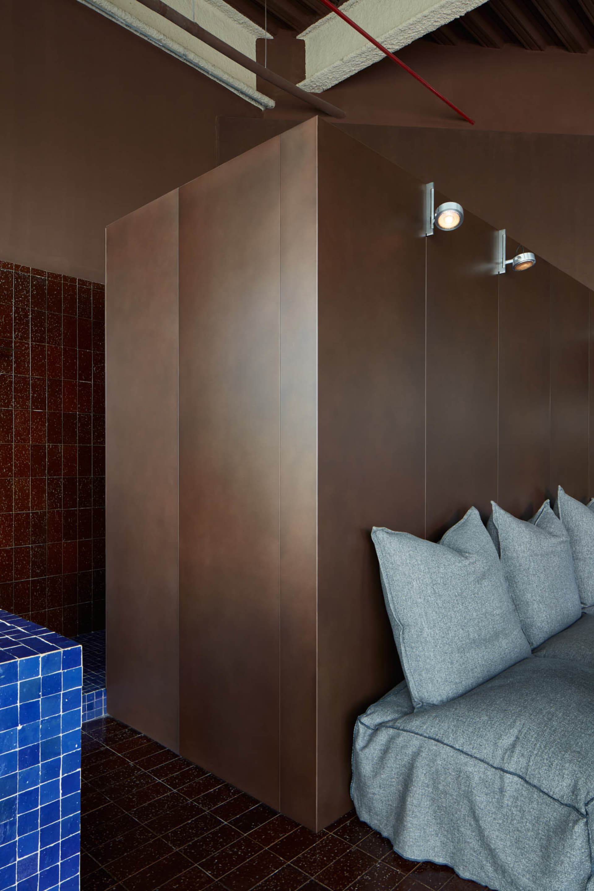 Modern bathroom with a brown cabinet, shower area, and a couch with two pillows, featuring a well-lit and comfortable design