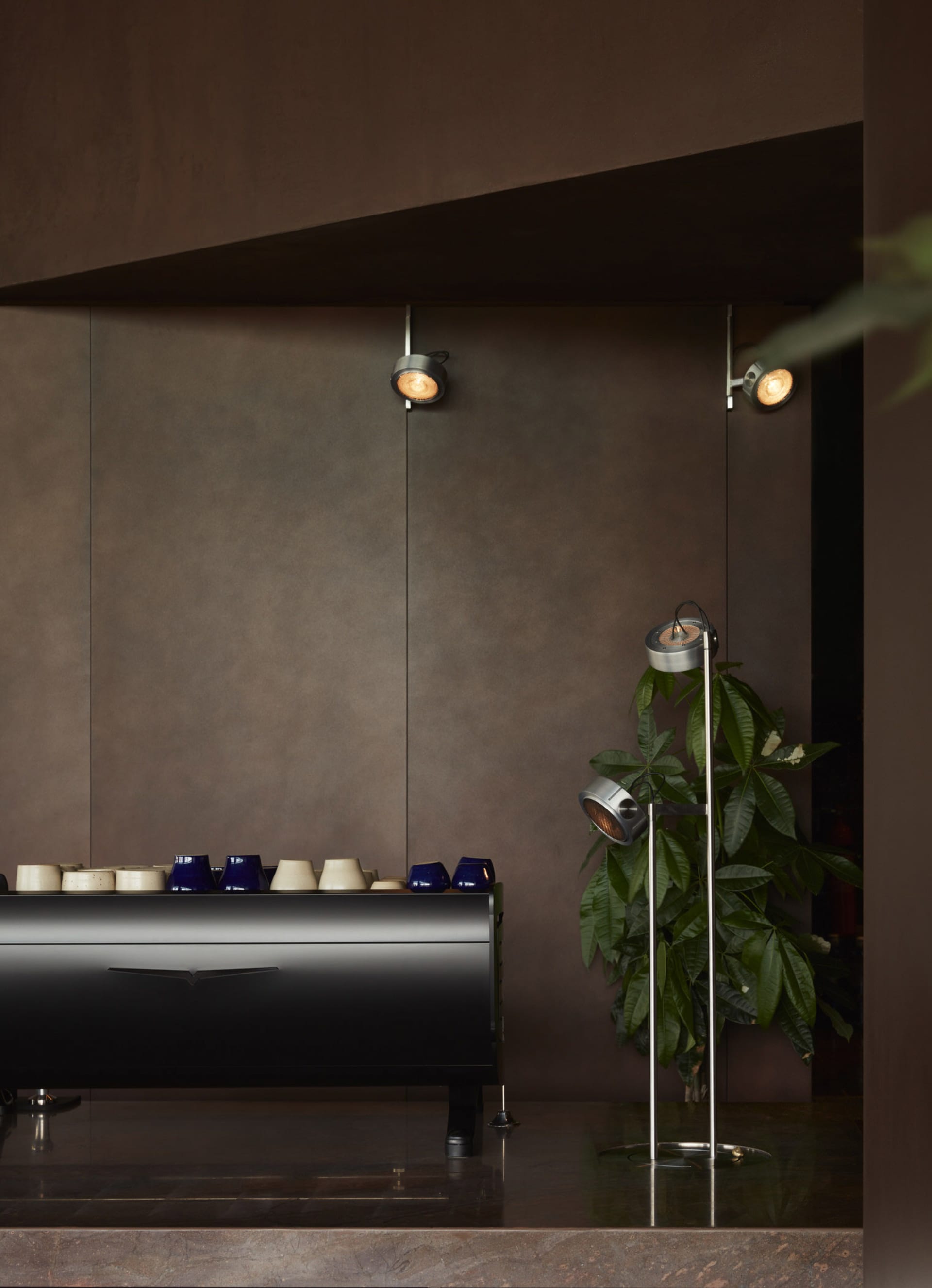 A kitchen or dining area with a black countertop featuring various bowls and cups, accompanied by two potted plants, creating a cozy atmosphere