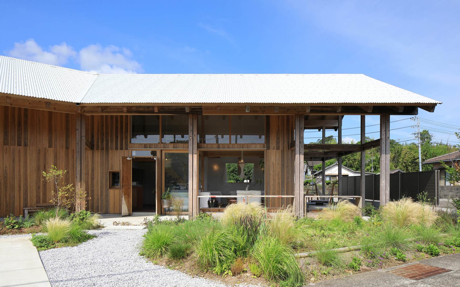 A modern house with a wooden exterior, a large deck, and potted plants, well-lit by natural sunlight