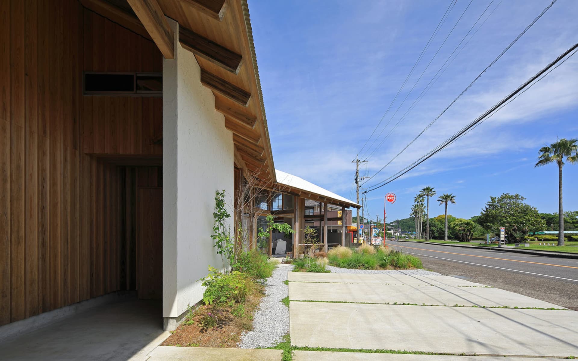 A modern building with a wooden exterior and a large window, set against a backdrop of trees and a bench in a public or commercial area