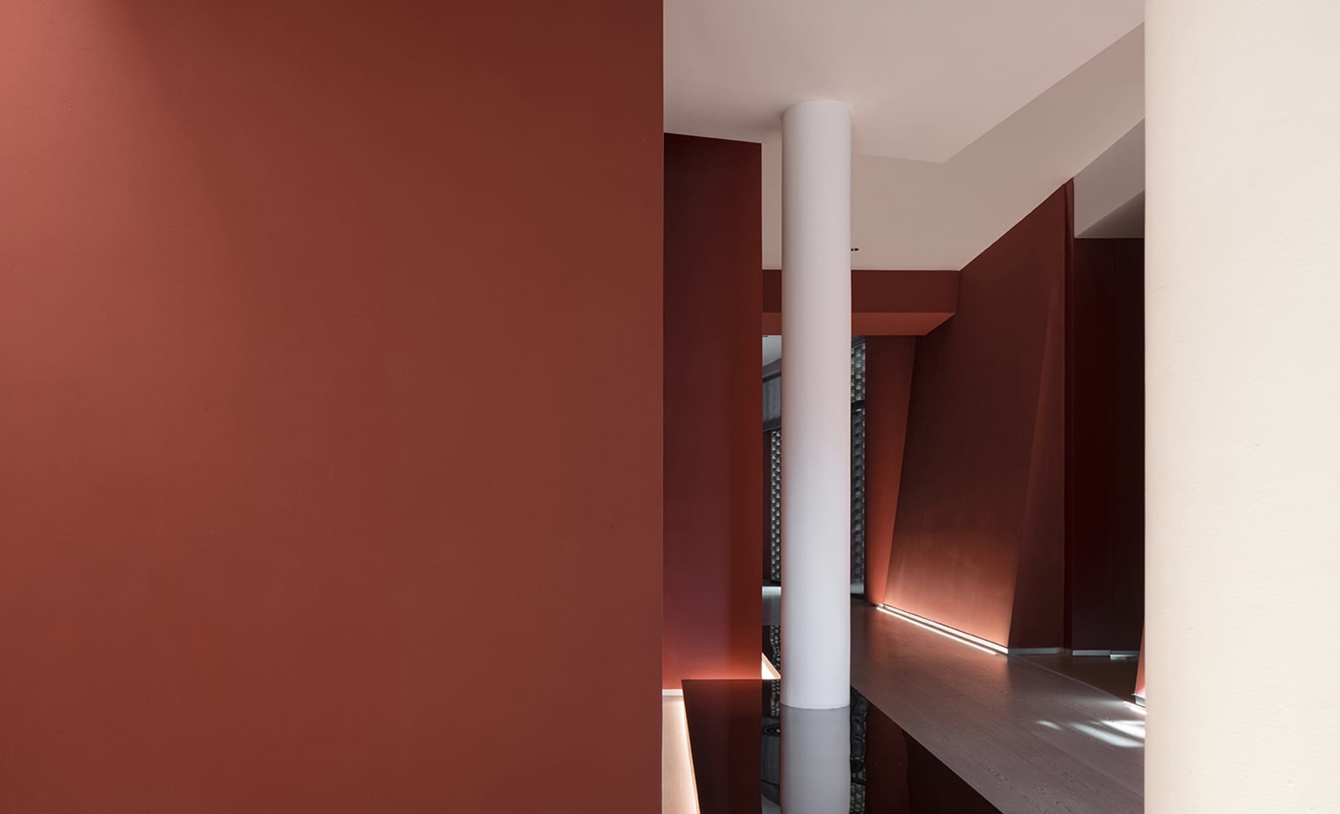 Narrow modern hallway with red walls, a white pillar, and natural light from a window