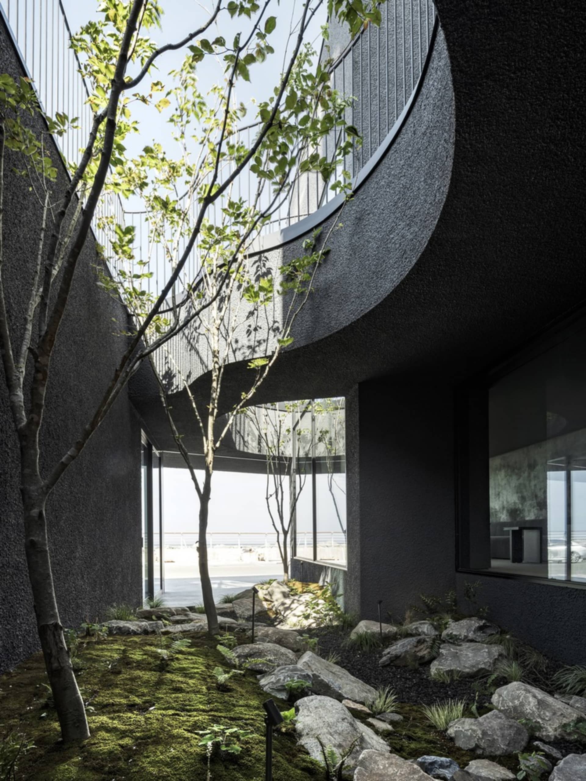 Modern house with a black exterior, spiral staircase, and a balcony on the second floor, surrounded by trees