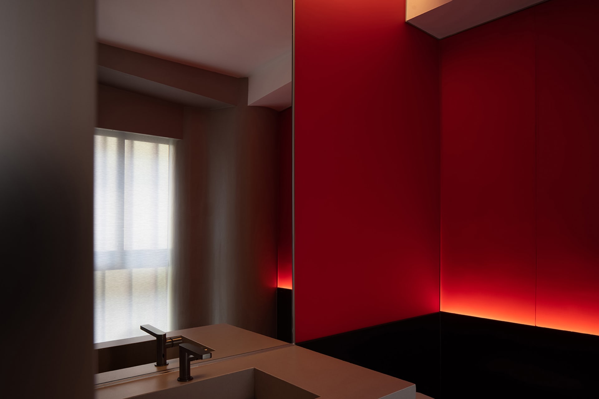 A minimalist bathroom with a red wall, a sink, and a mirror, creating a bold atmosphere