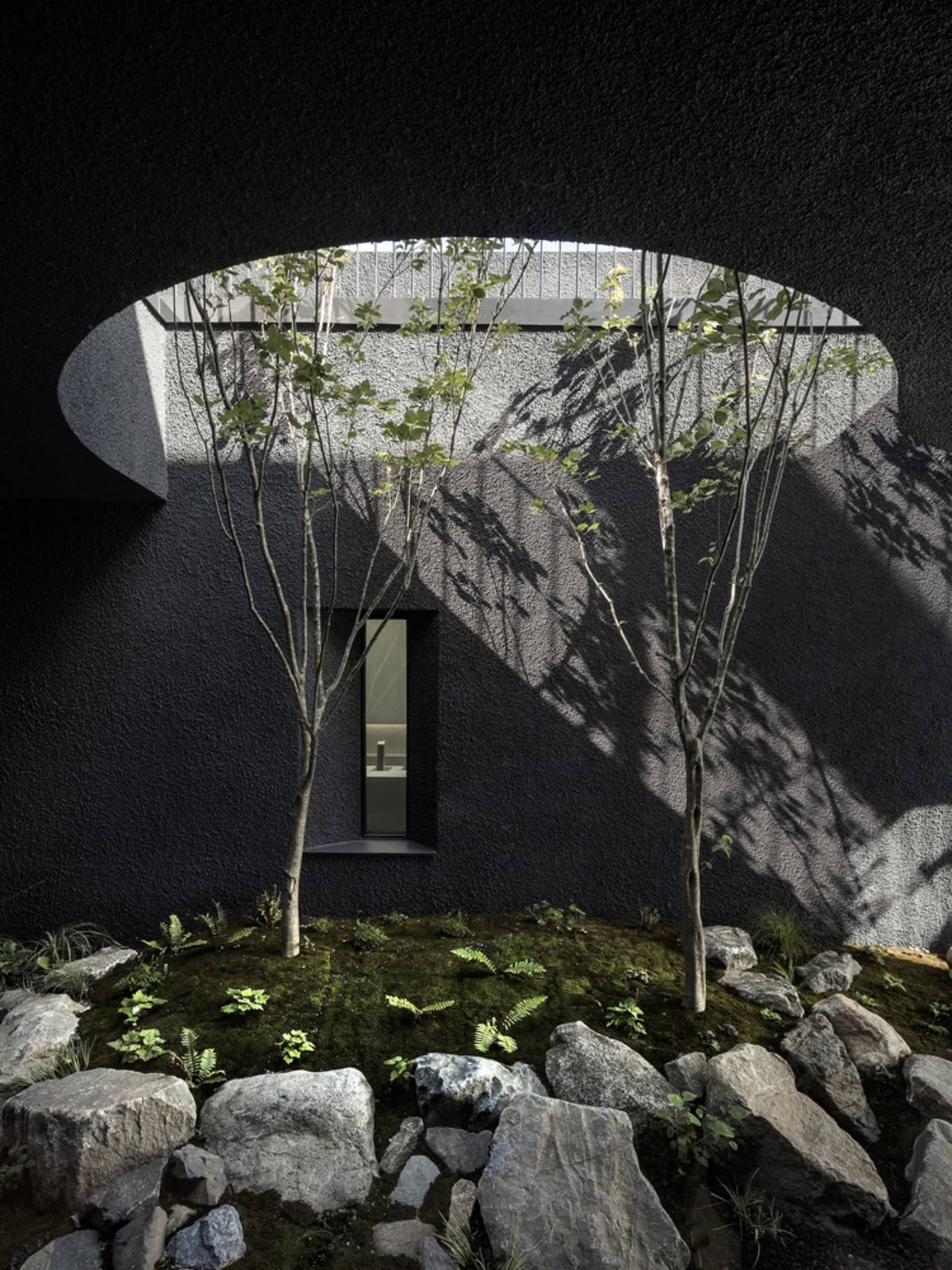 A modern house with a black exterior, surrounded by two trees and rocks, set in a well-lit scene