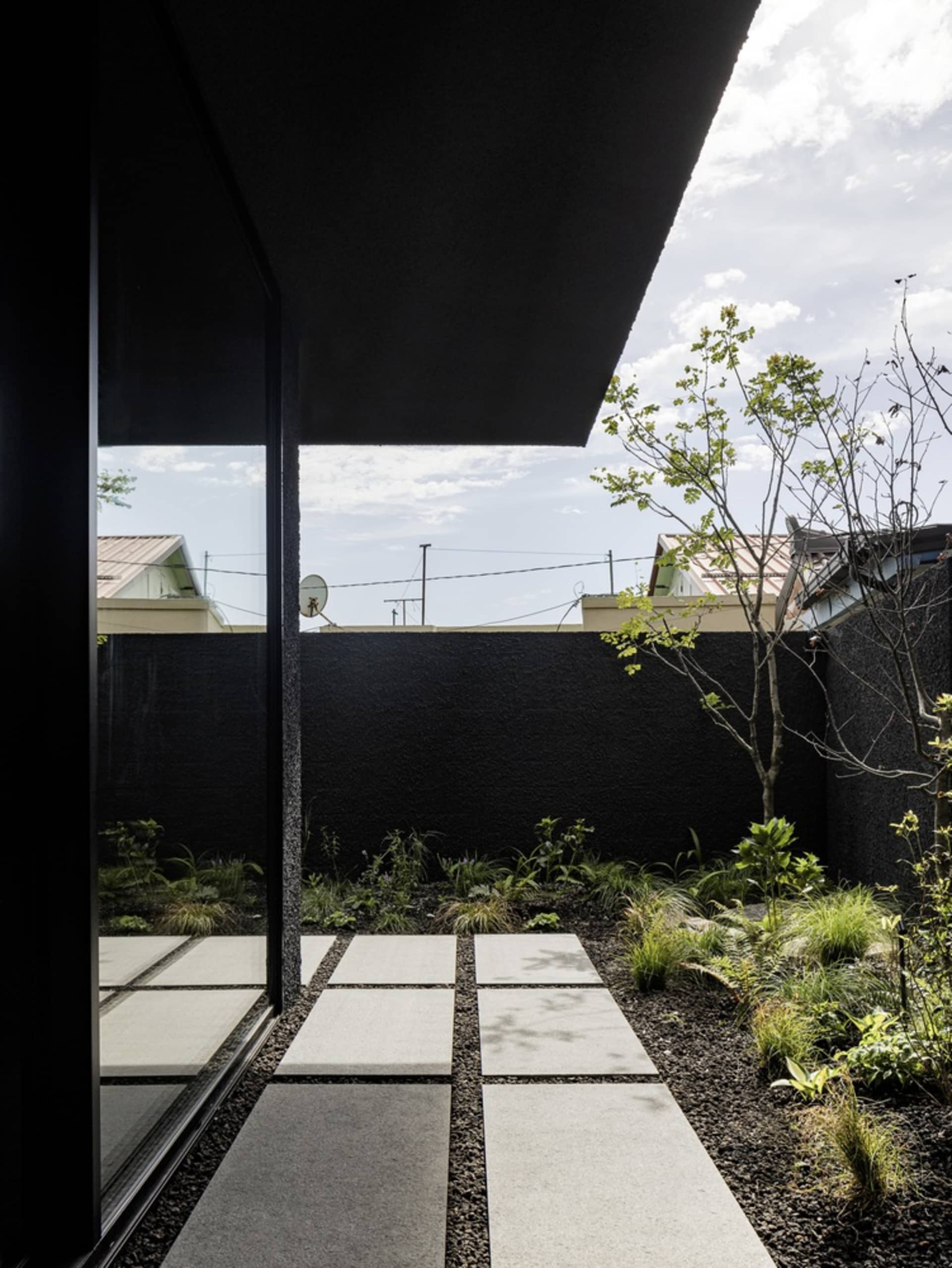 A modern outdoor patio with a black wall, glass door, potted plants, and a TV mounted on the wall, creating a lively and inviting atmosphere