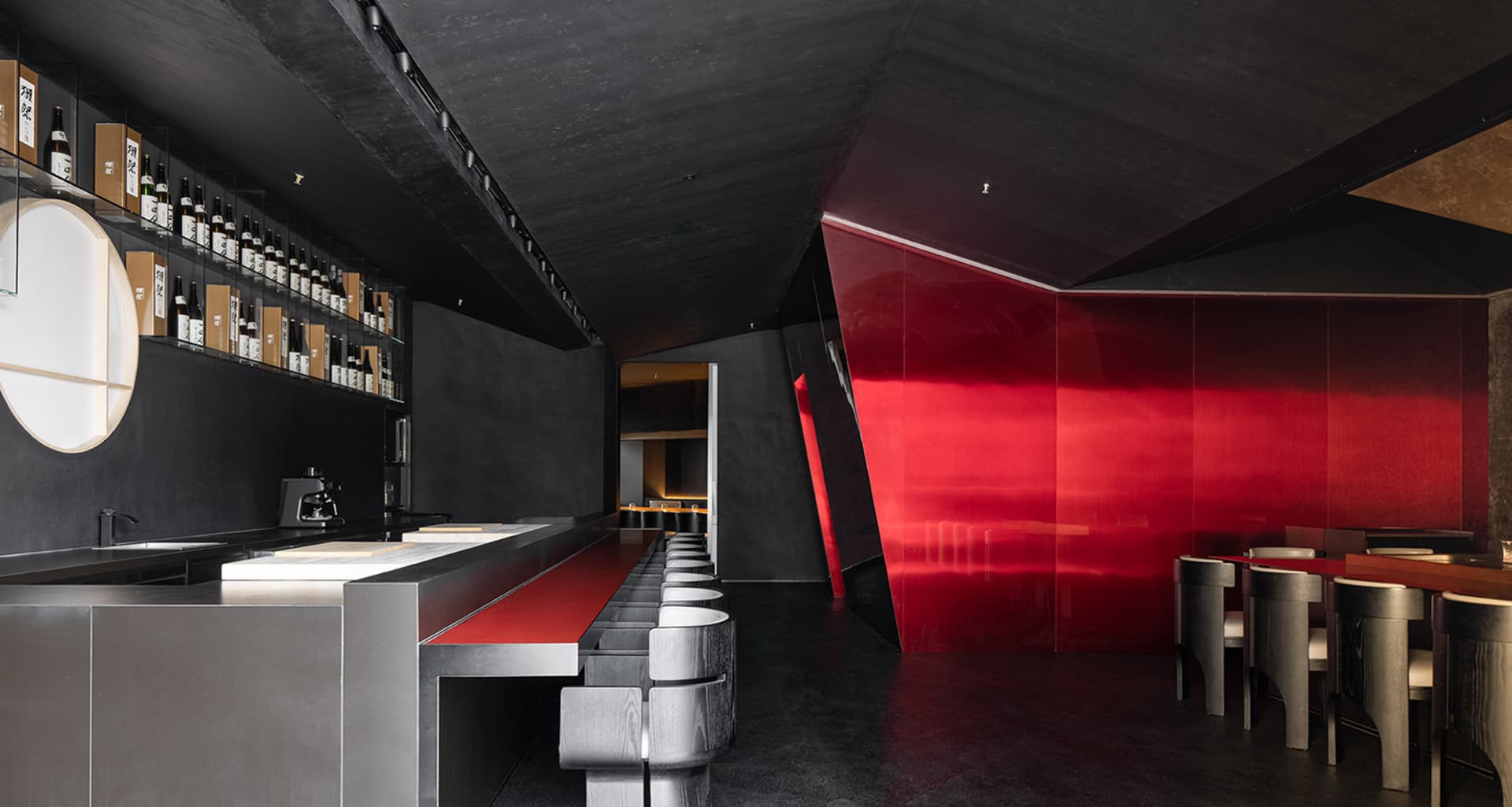 Modern restaurant interior with a long counter, red accents, and books scattered throughout, exuding a stylish and contemporary vibe
