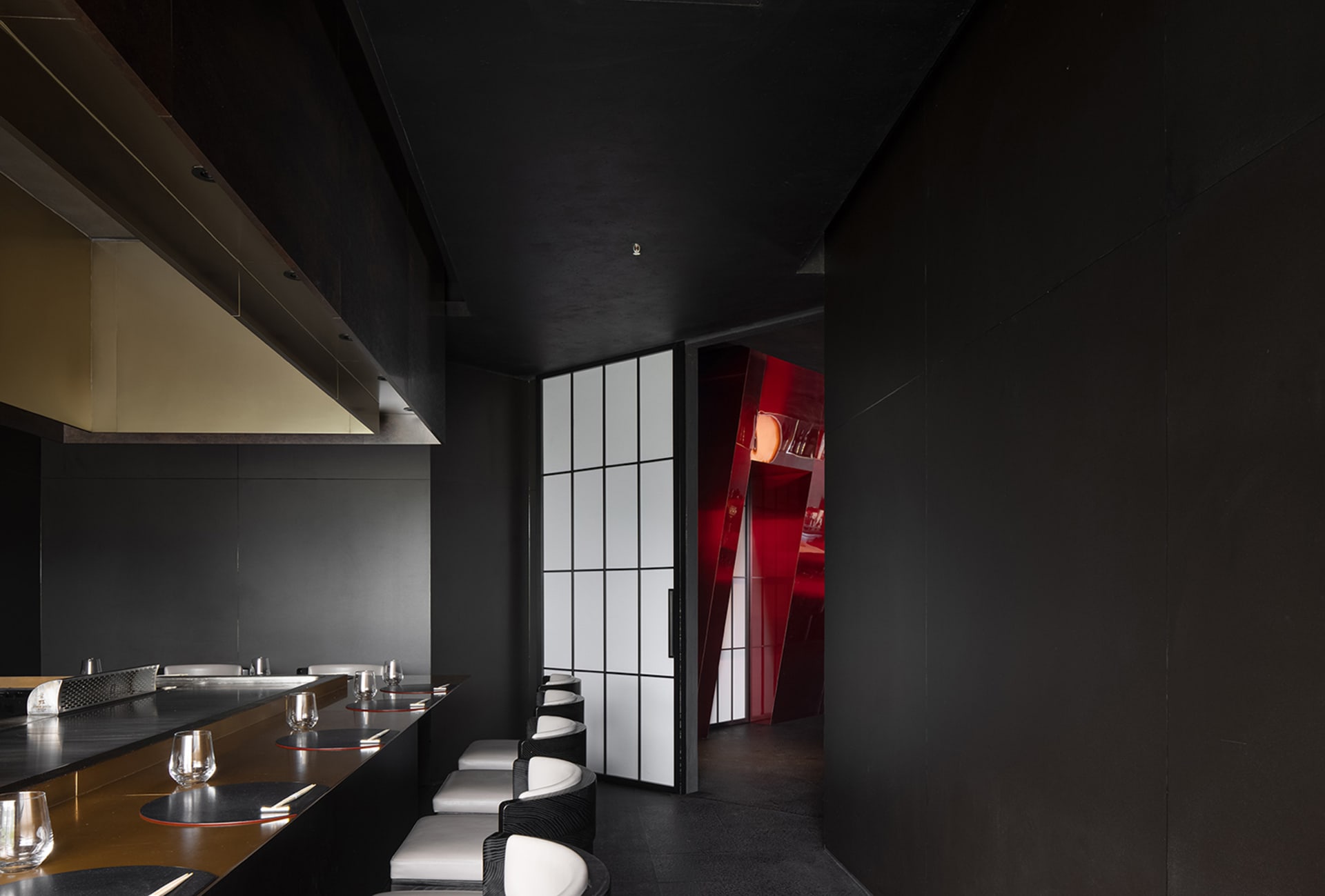 Empty restaurant interior with black walls, red doorway, and chairs placed around the dining area