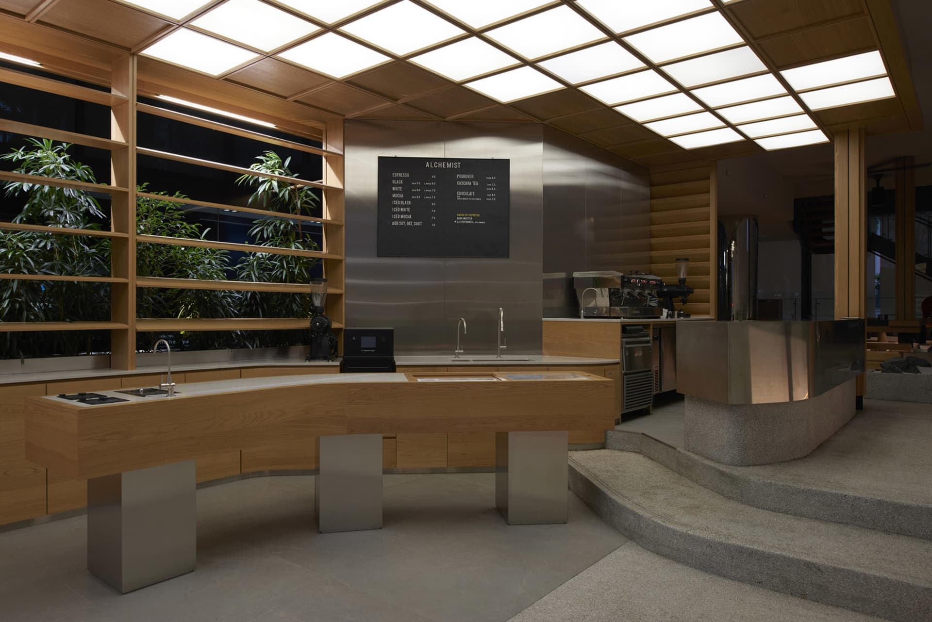 A modern restaurant counter with two sinks and a menu board, surrounded by potted plants in a clean and well-organized space