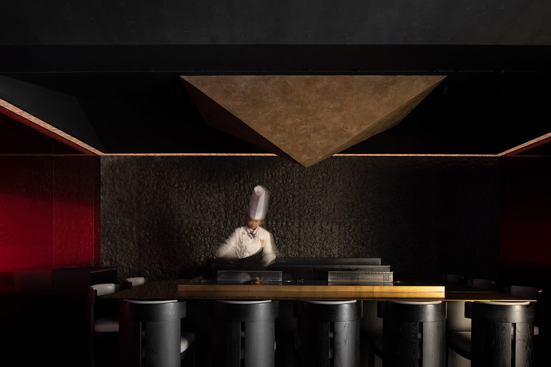 A busy restaurant kitchen with a chef preparing food on a grill, surrounded by chairs and a dining table