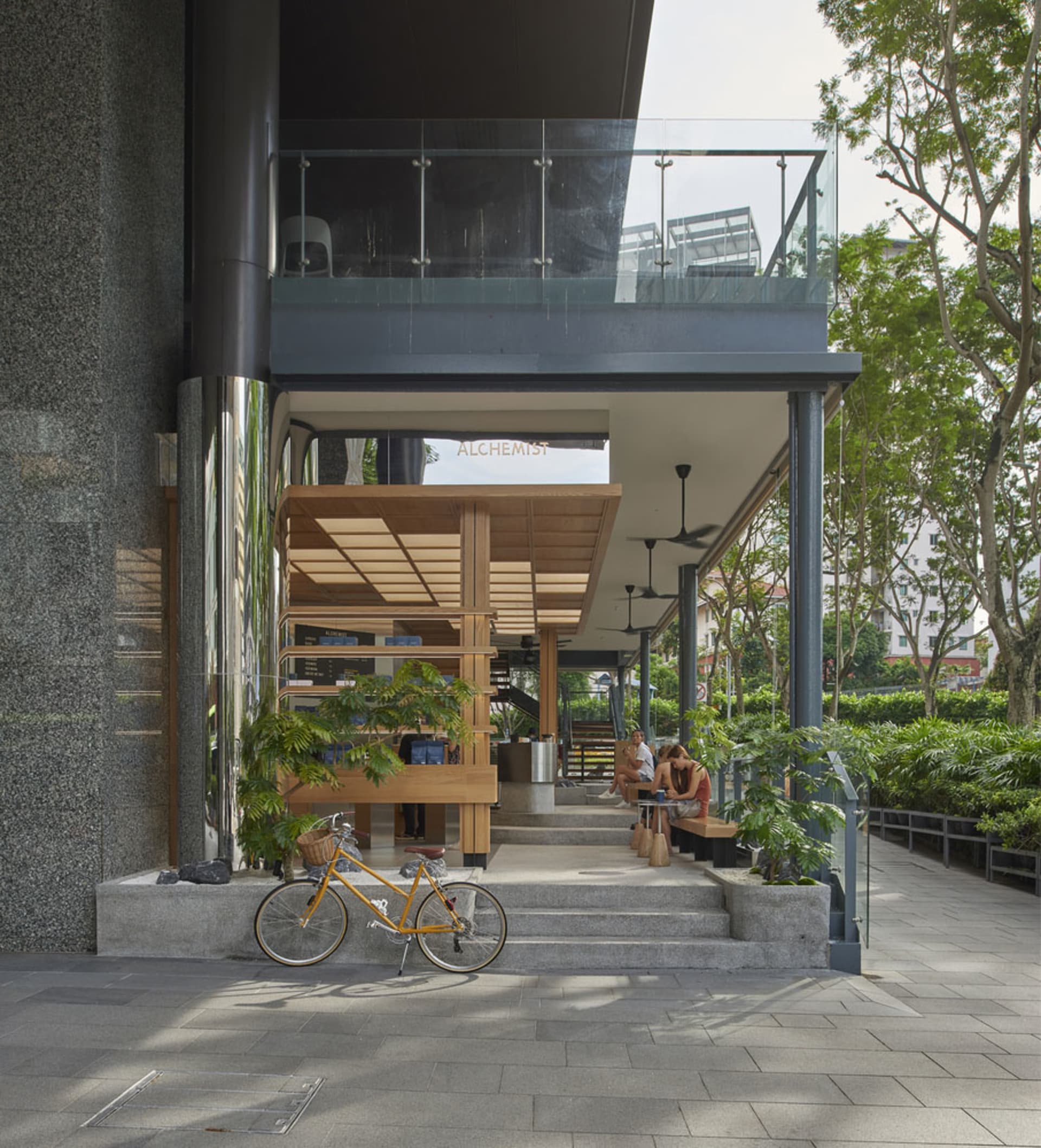 Modern interior space with a large glass wall, wooden frame, potted plants, and two chairs, featuring a contemporary design with natural elements
