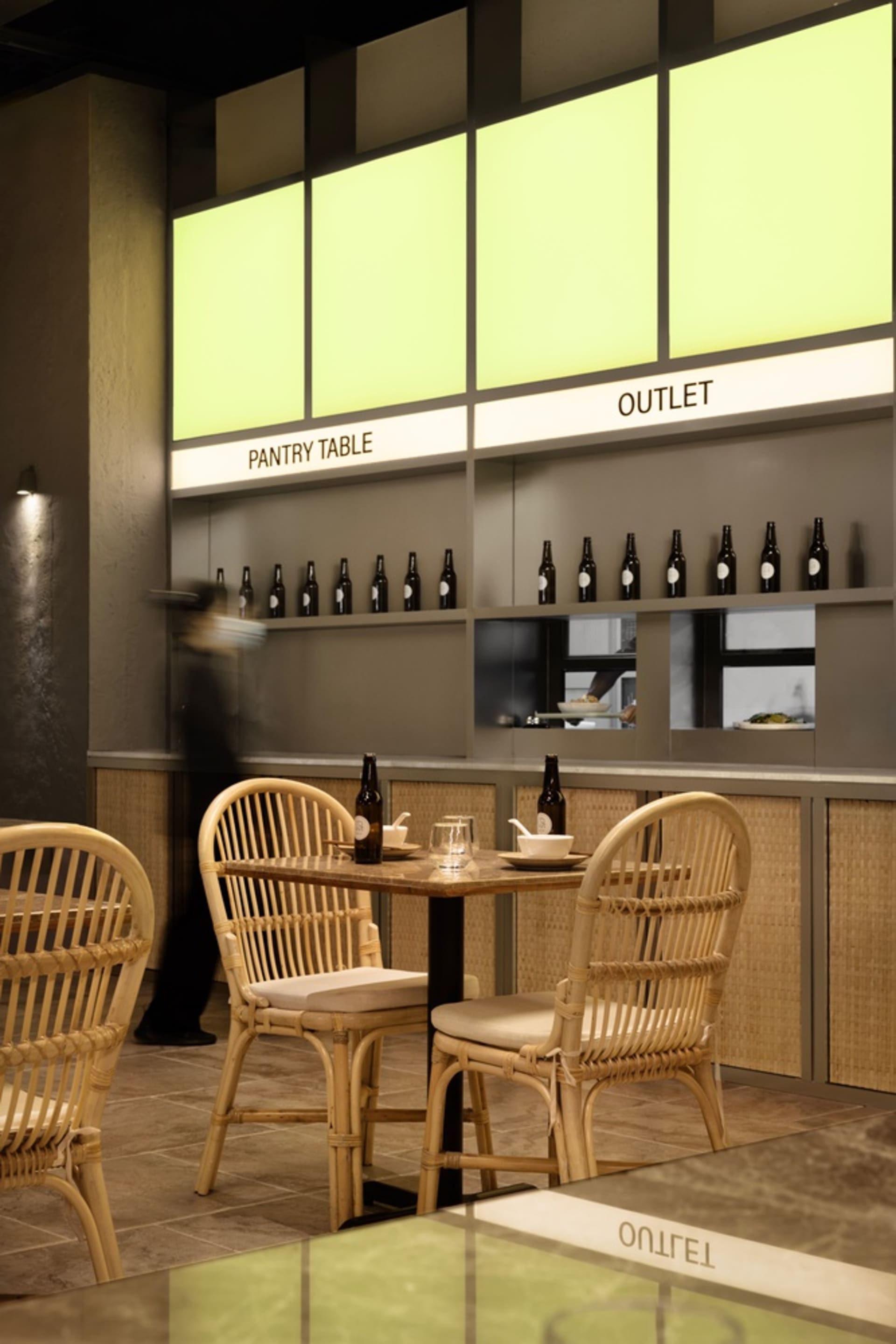 A cozy restaurant dining area with wicker chairs, tables, and bottles, set in a warm and inviting atmosphere