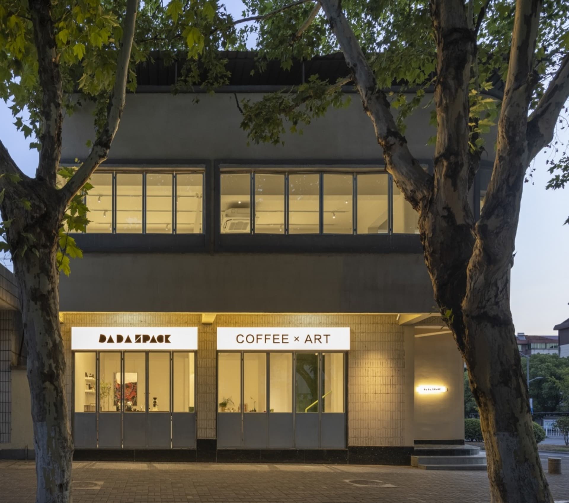 A modern building with two storefronts, a coffee shop, and an art gallery, featuring large windows, potted plants, chairs, and dining tables