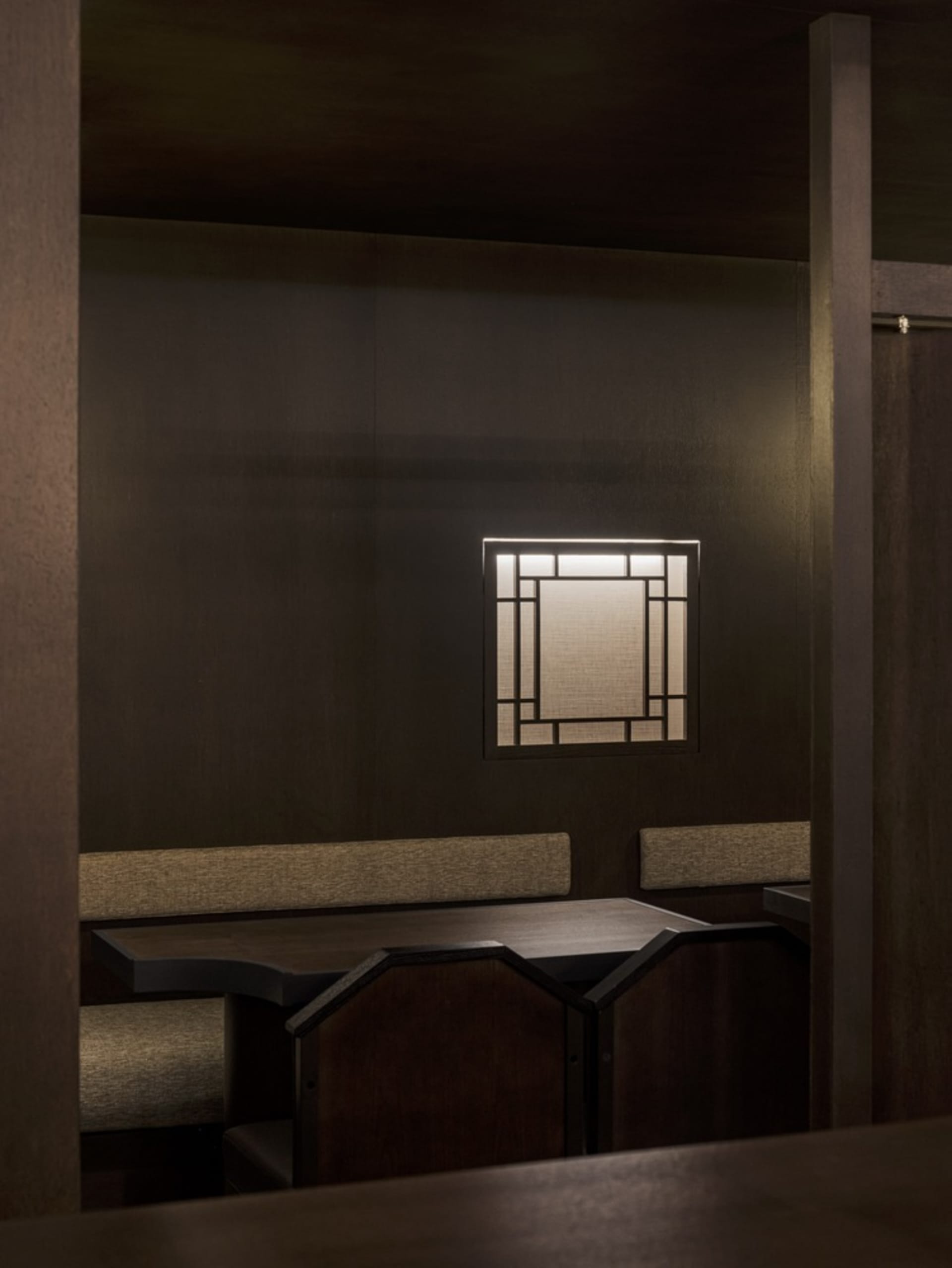 Small room with wooden walls and floors, featuring a dining table and benches, dimly lit for a cozy atmosphere