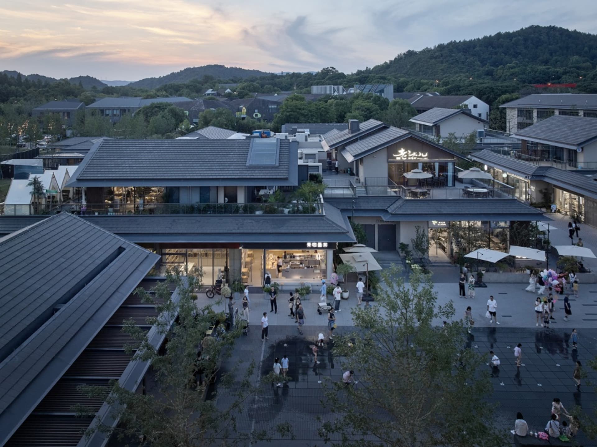 Aerial view of a shopping center at night with various buildings and greenery, featuring a mix of modern and traditional architecture and bustling activity