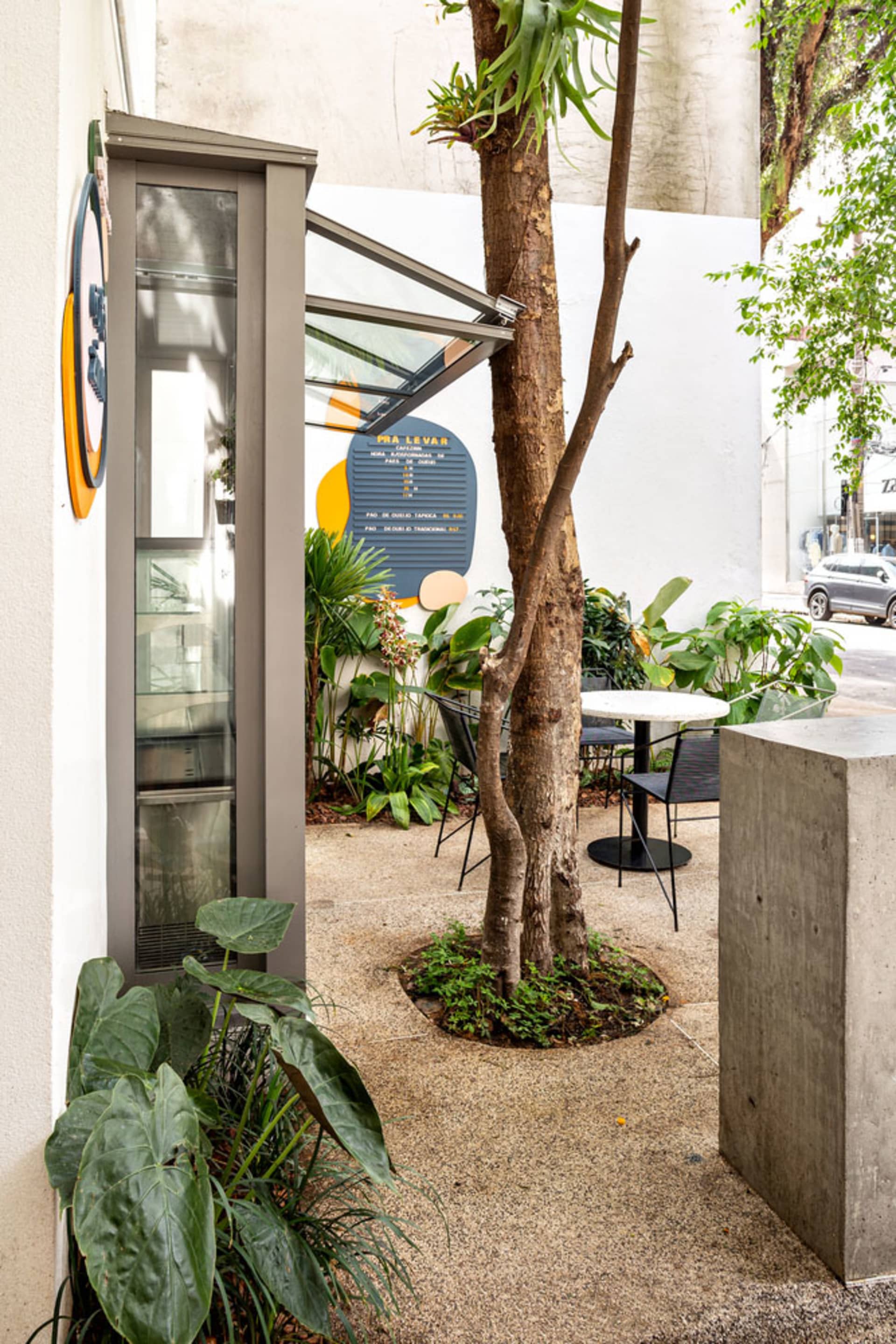 Outdoor dining patio with a stone floor, a dining table, and potted plants, set against a backdrop of parked cars
