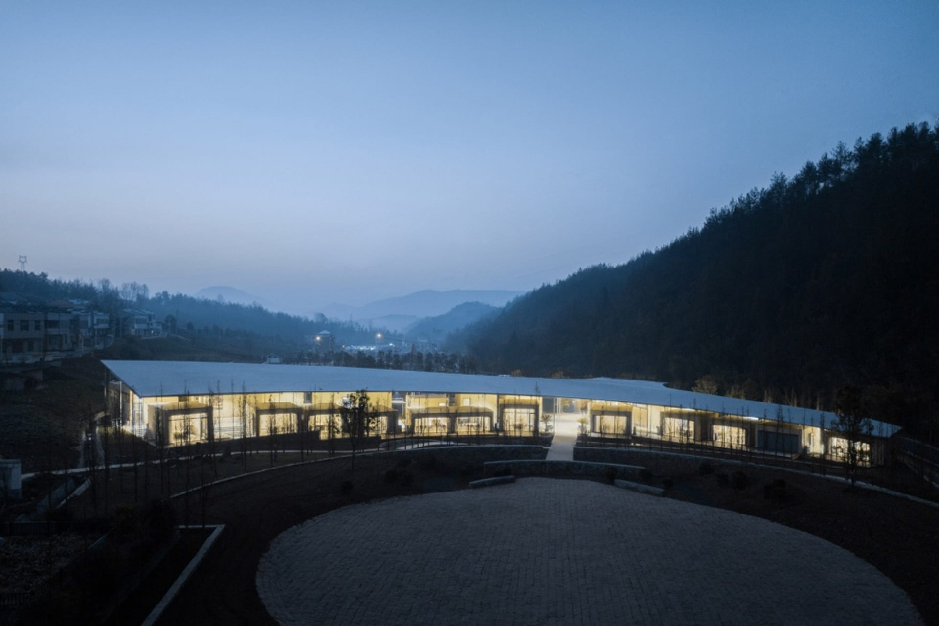 A modern building with a circular shape and lit windows, set against a dark background