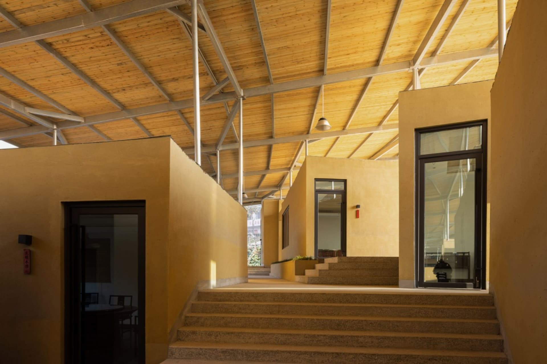 A two-story house with a yellow exterior wall, featuring windows on both levels and a wooden staircase with a railing, conveying a comfortable and welcoming living environment
