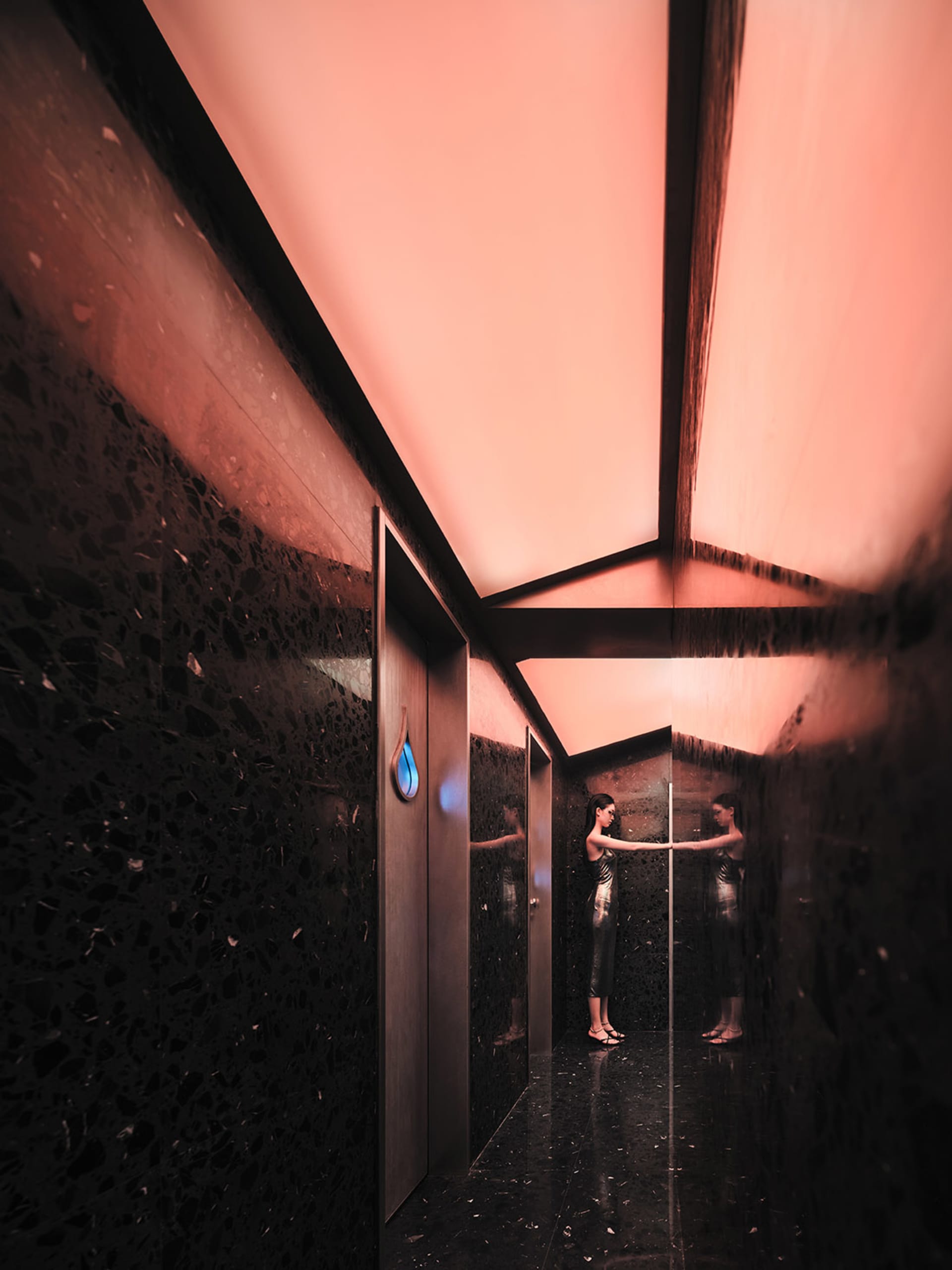 A woman stands in front of a mirror in a bathroom with a black tile wall behind the mirror, giving it an elegant appearance