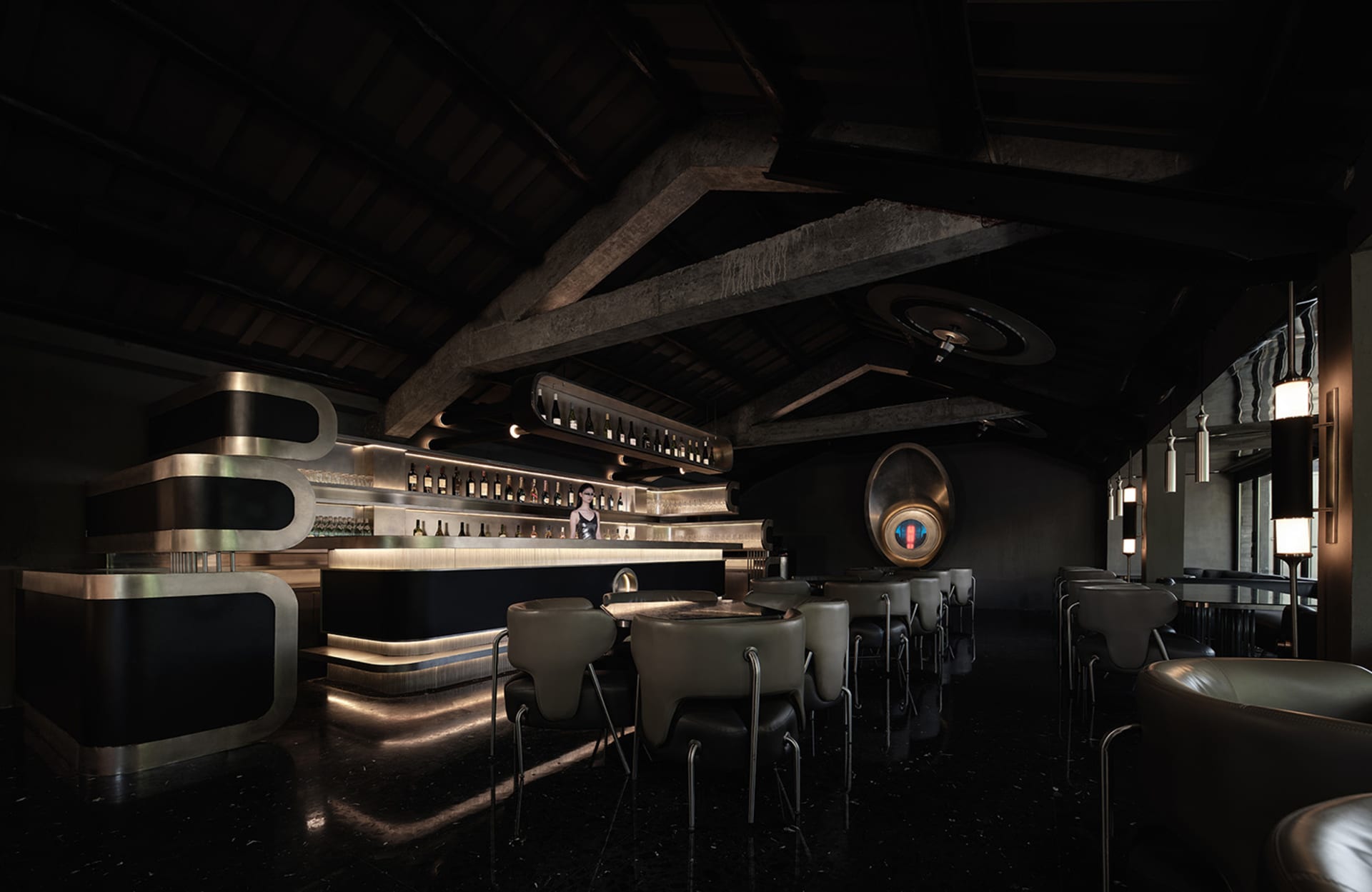 A dark and intimate bar area with a wooden counter and multiple barstools, lined with bottles and creating a cozy ambiance