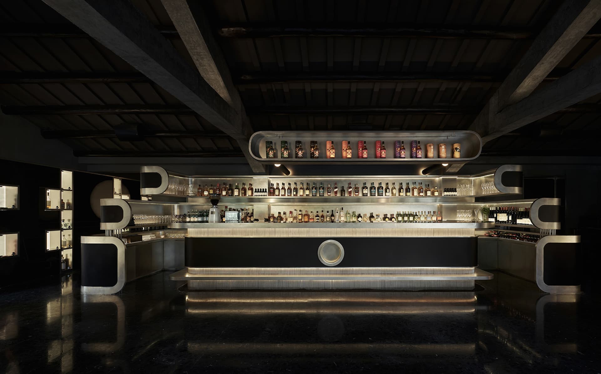 A sophisticated bar with a large display of liquor bottles on a counter, accompanied by wine glasses, suggesting a high-end establishment or luxury hotel