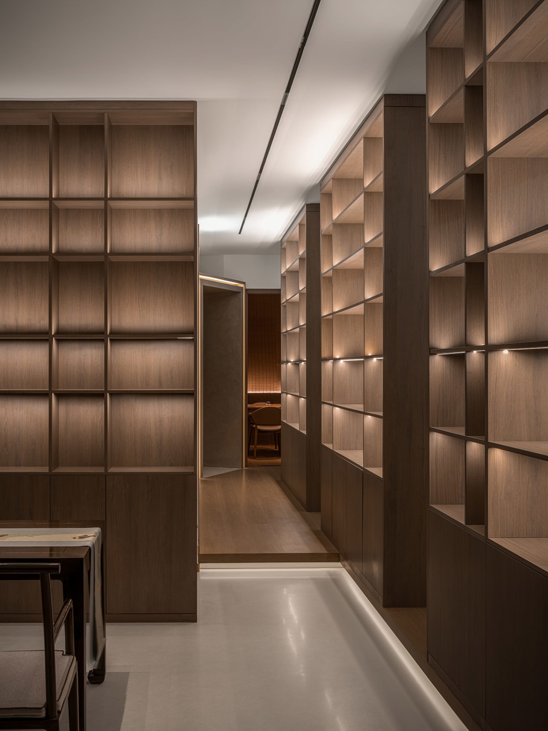 A calm and organized hallway with wooden walls and floors, lined with bookshelves and a chair, showcasing a collection of books