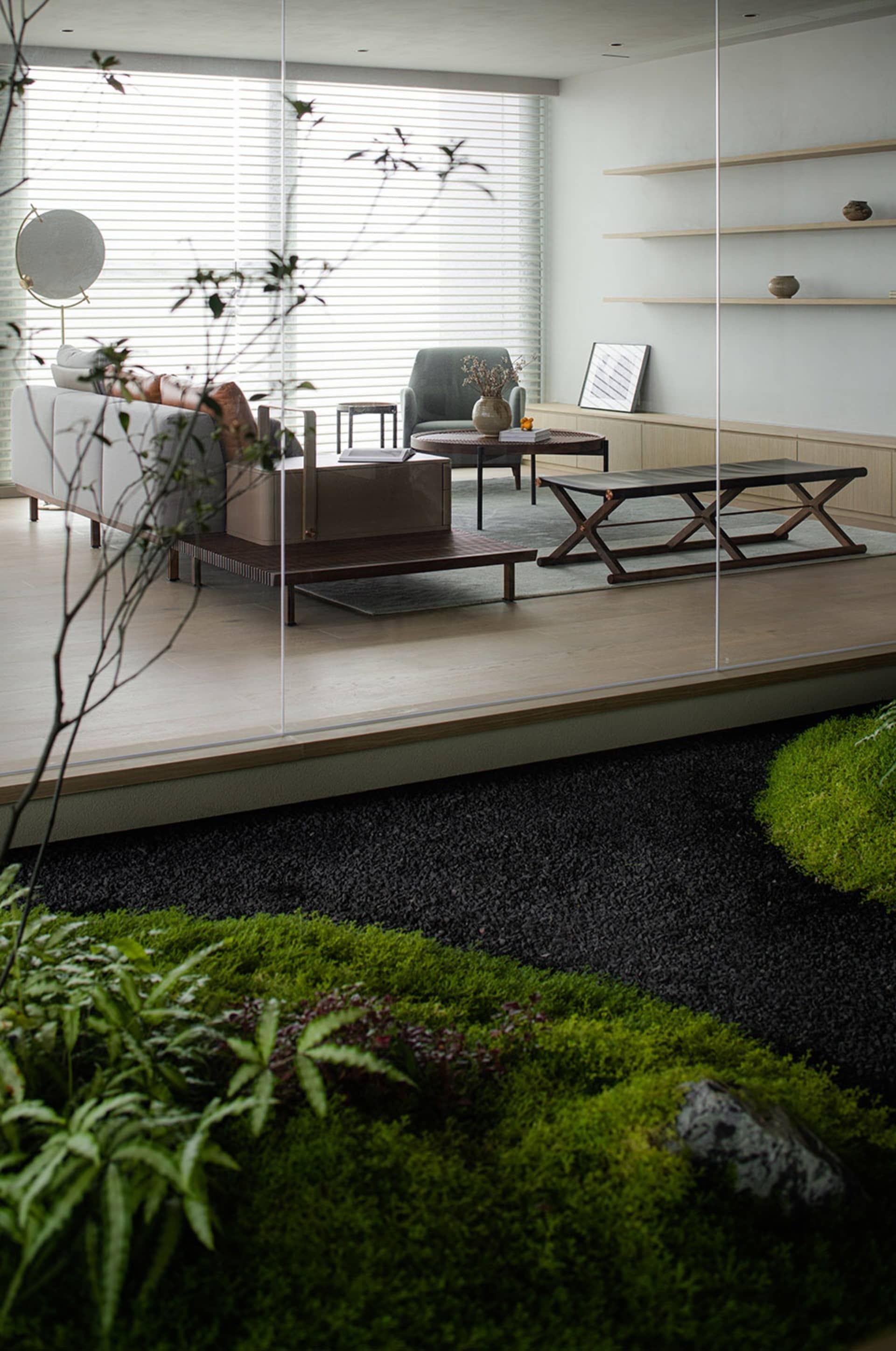 Open living area with a couch, chairs, dining table, and potted plants, surrounded by glass walls and natural light
