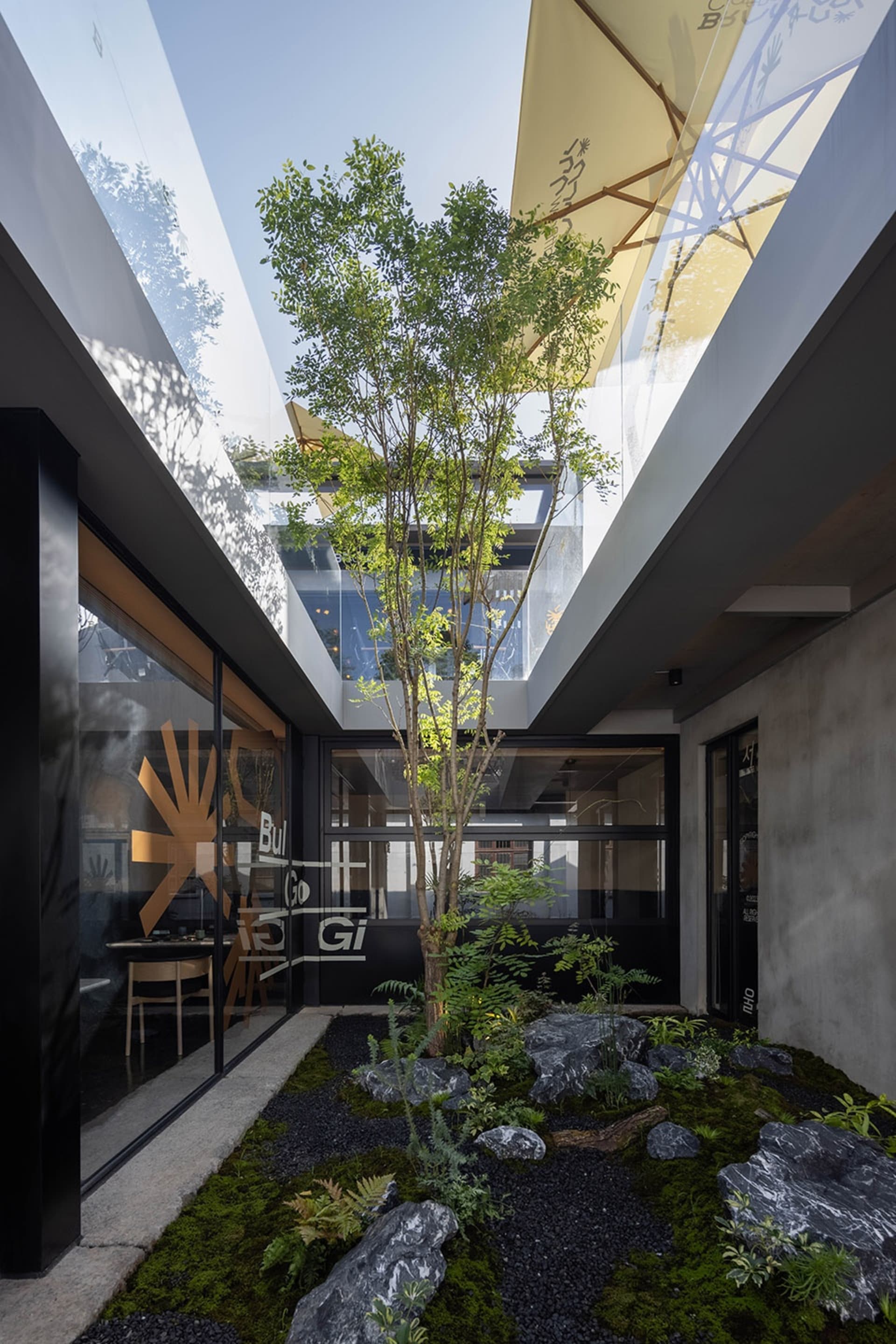 A calm and inviting indoor space with a large tree in the center, surrounded by chairs and two dining tables, with a touch of nature added to the interior design