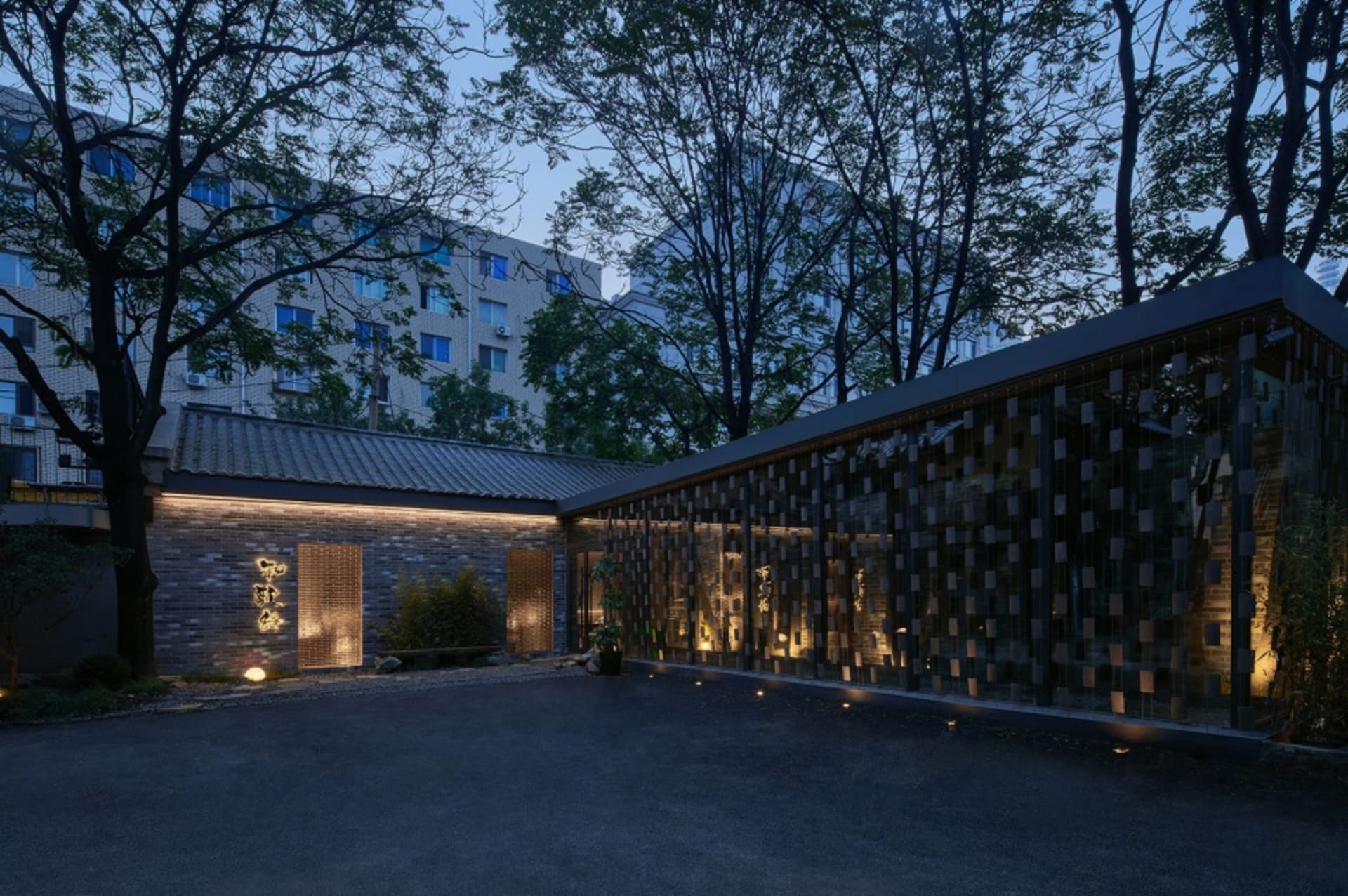 A modern building with a glass wall featuring a brick pattern, a stone facade, and a concrete structure, with windows and curtains